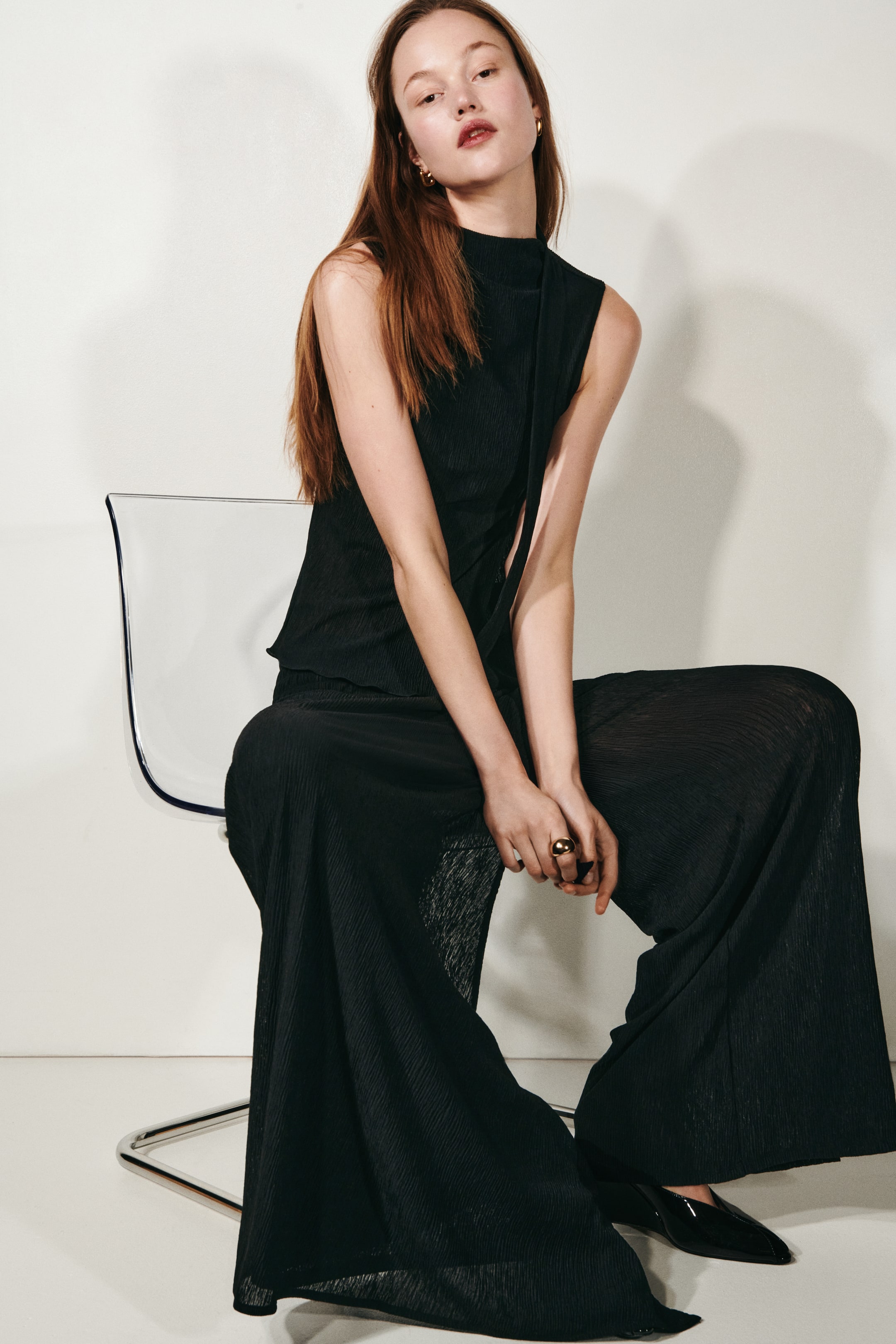 Voir une image plus grande: Un haut sans manches noir plissé avec un col cheminée et un panneau avant drapé, associé à un pantalon noir plissé à jambes larges assorti. Le pantalon tombe avec fluidité jusqu'au sol.