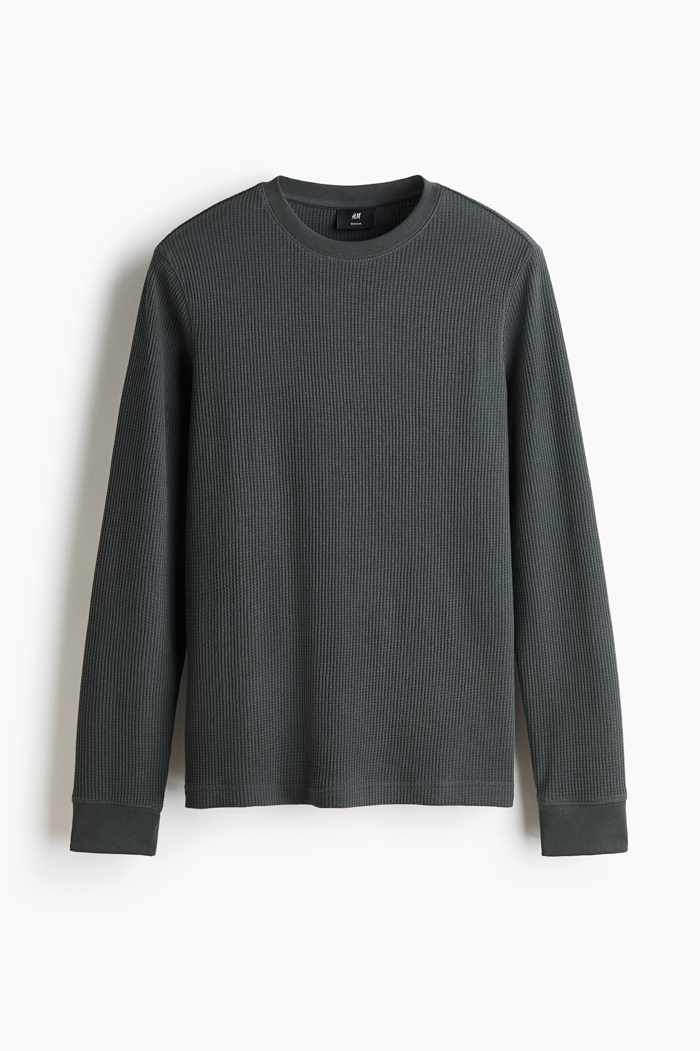 Un t-shirt Ã  manches longues gris foncÃ© en jersey de mÃ©lange coton gaufrÃ© est portÃ© par le mannequin. Le haut prÃ©sente un col rond cÃ´telÃ© et des poignets cÃ´telÃ©s, et il est assorti Ã  un jeans beige pÃ¢le.