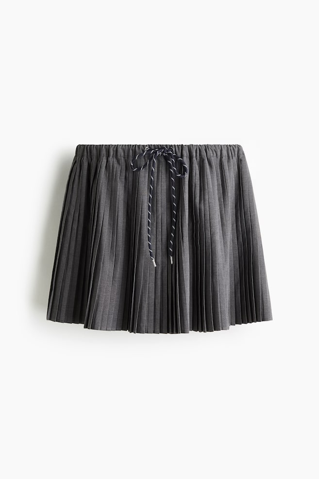 A gray flared mini skirt is being shown from the FRONT, displaying a pleated weave and a flared silhouette. An elasticated, drawstring waist is featuring a black and white striped cord that is forming a bow at the center, with its ends displaying silver-toned tips. - 1