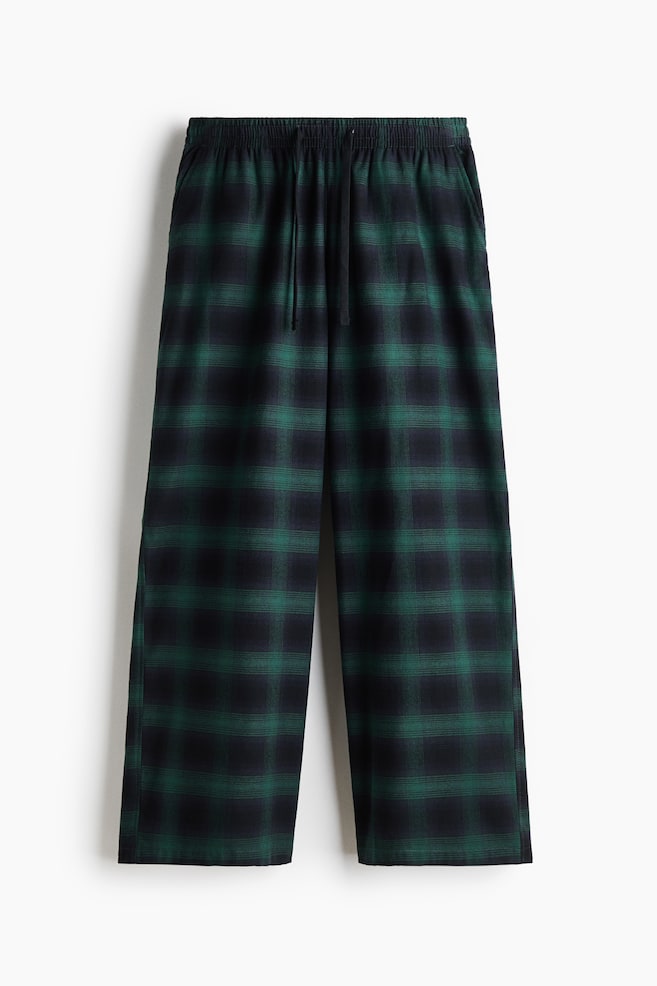 Un pantalon large Ã  carreaux verts et noirs est suspendu vu de face, avec une taille Ã©lastiquÃ©e et un cordon de serrage noir. - 1