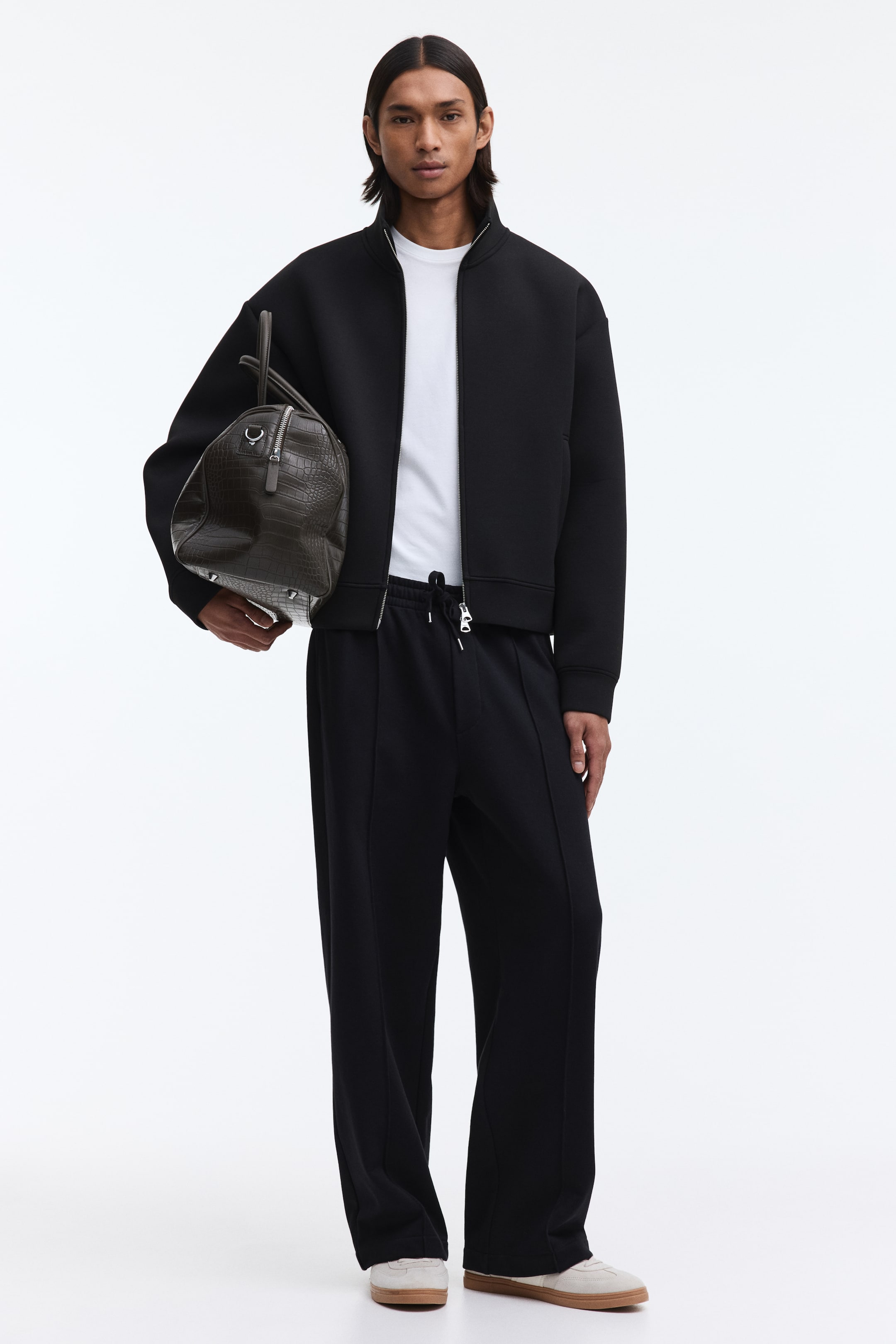 View larger image: A black bomber jacket crafted from structured fabric features a stand-up collar, a full-zip front, and a relaxed, cropped fit, showcased over a white t-shirt and paired with black trousers.