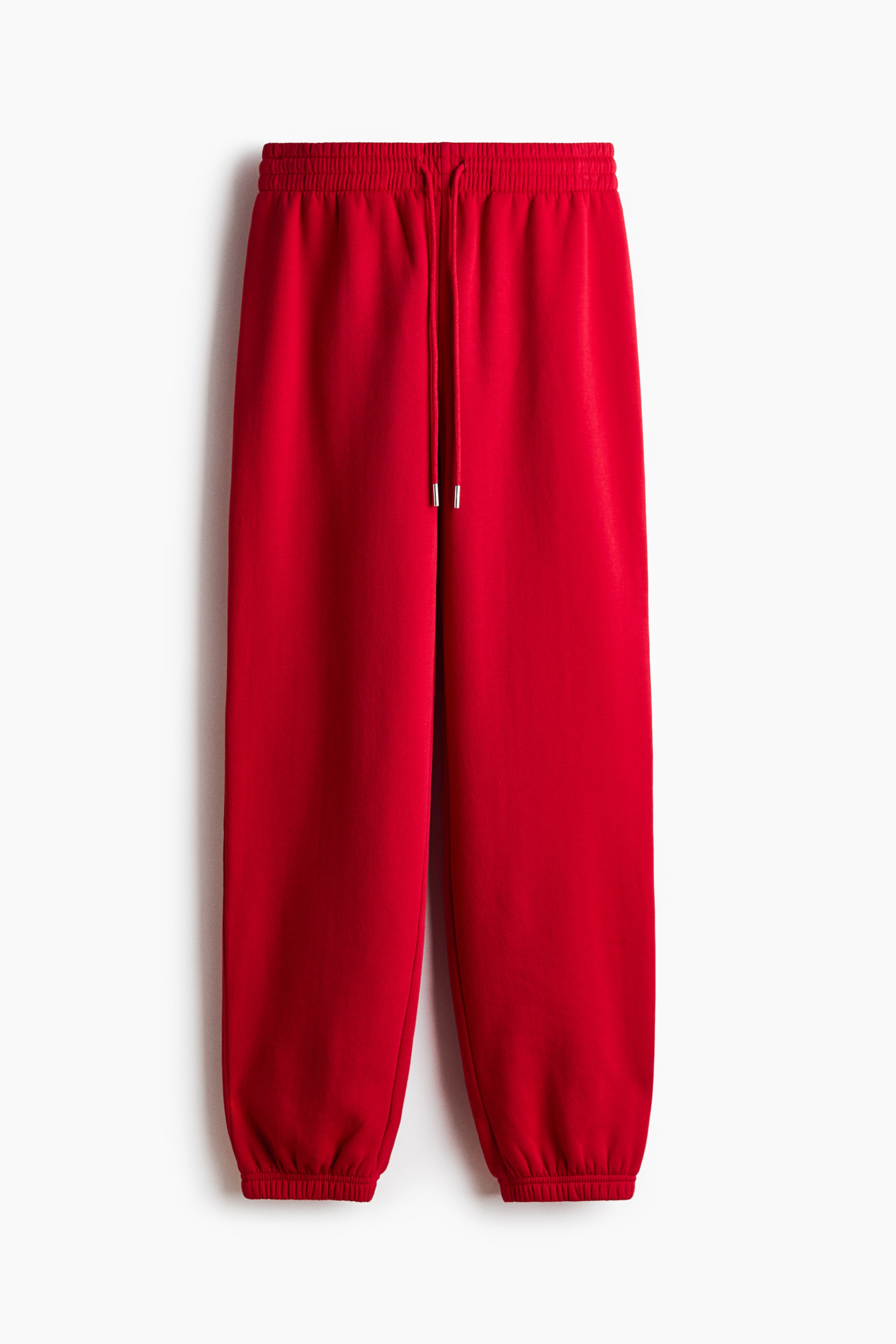 View larger image: Red track pants hang facing forward, featuring a high, covered elastic waistband with a matching drawstring finished with silver tips. The relaxed-fit legs taper down to gathered, elasticized hems.