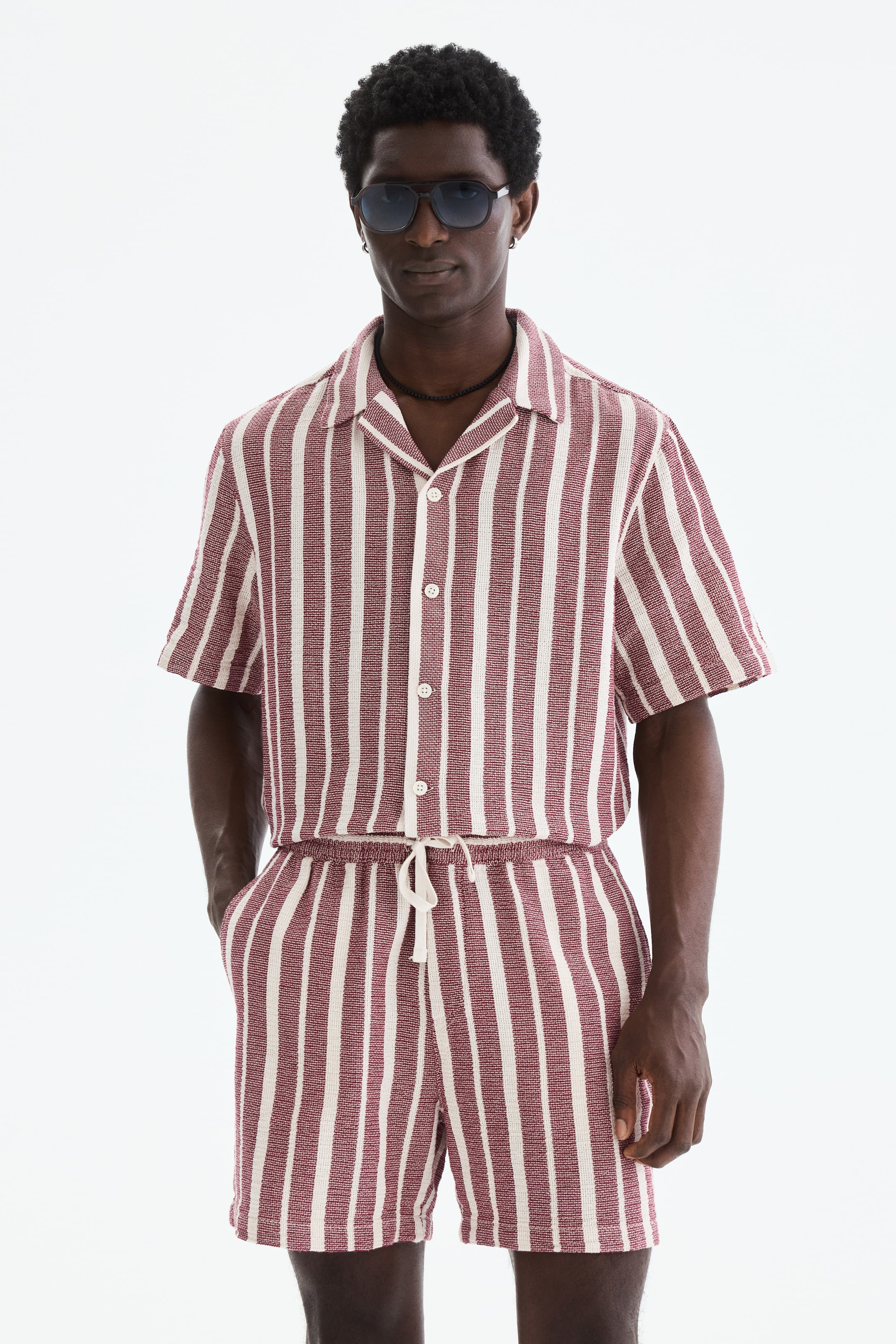 View larger image: A coordinating short-sleeved shirt and shorts set showcases textured vertical maroon and cream stripes. The shirt features a camp collar and a button-front closure, while the shorts are designed with an elasticated drawstring waist and pockets.