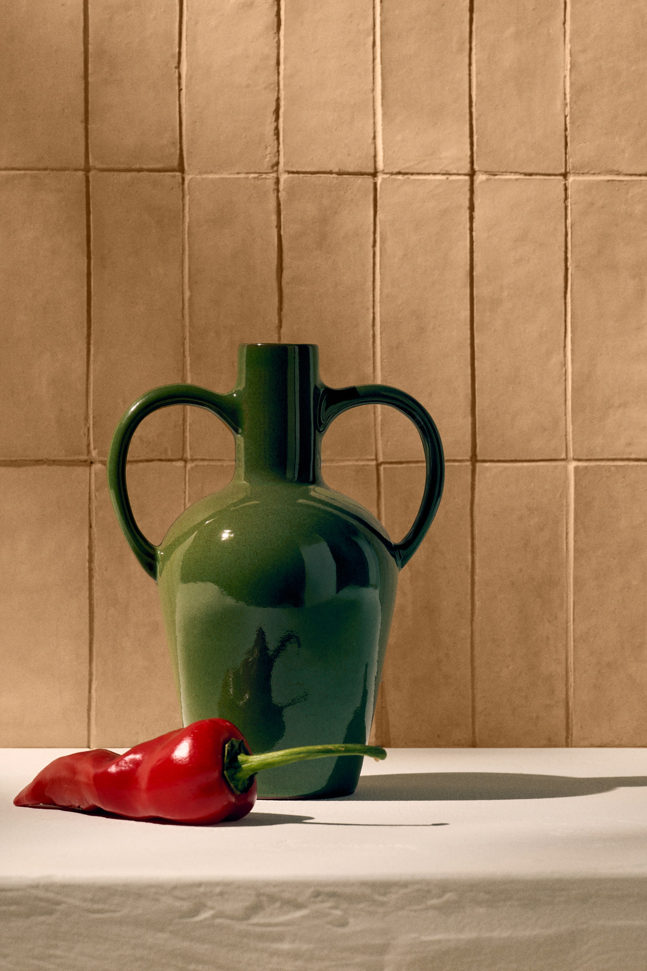 View larger image: A green vase showcasing a rounded body with a narrow opening and two side handles. It boasts a glossy, reactive glaze finish, giving it a distinctive appearance.