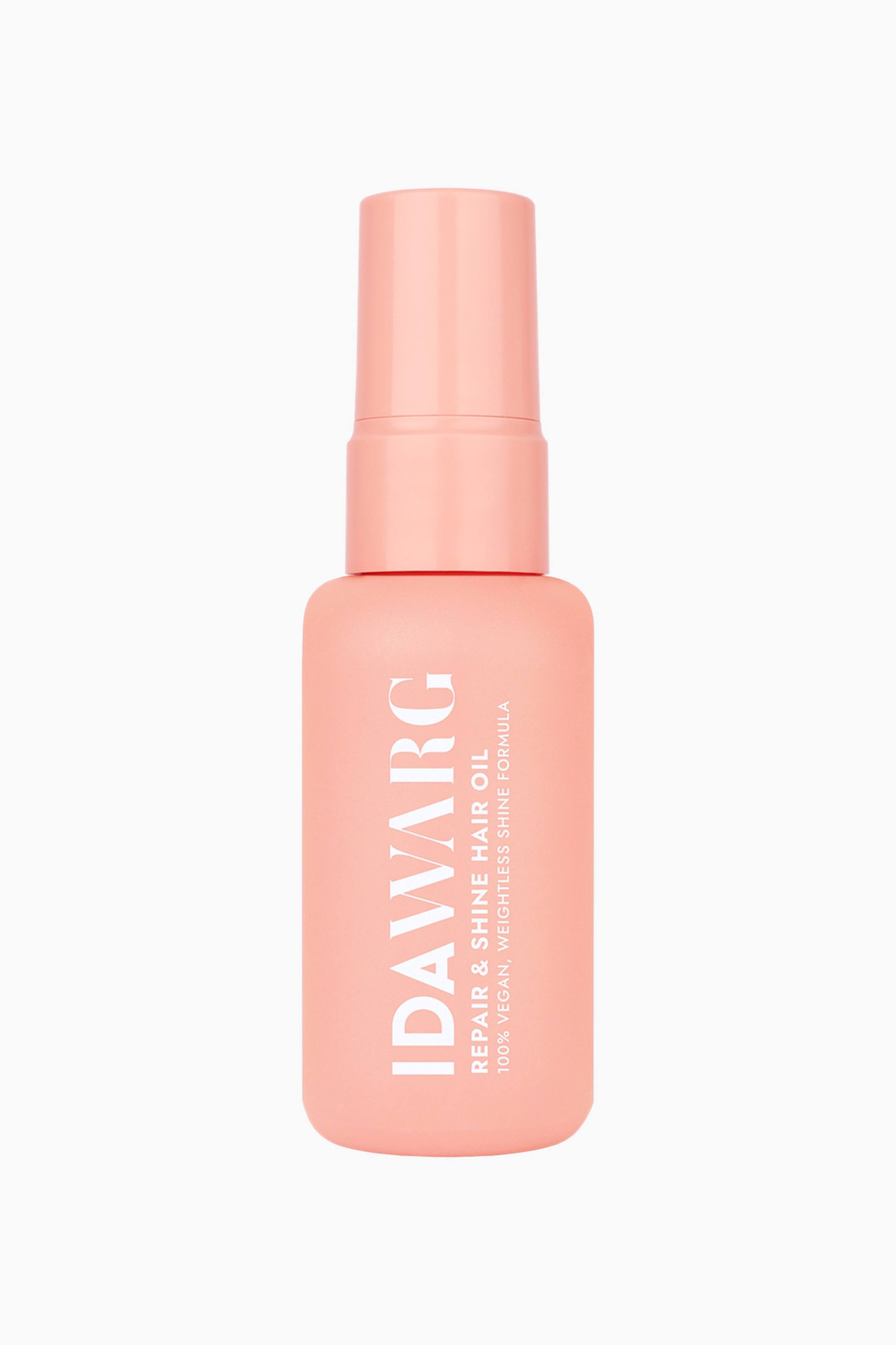 Größeres Bild ansehen: Eine matte Pfirsich-Haarölflasche steht aufrecht und zeigt nach vorne. Auf der linken Seite ist in weißem vertikalem Text "IDAVARG" zu sehen, mit "REPAIR & SHINE HAIR OIL" und "100% VEGAN, WEIGHTLESS SHINE FORMULA" in kleinerem weißen horizontalem Text. Die Flasche ist mit einem passenden Pfirsichverschluss versehen.