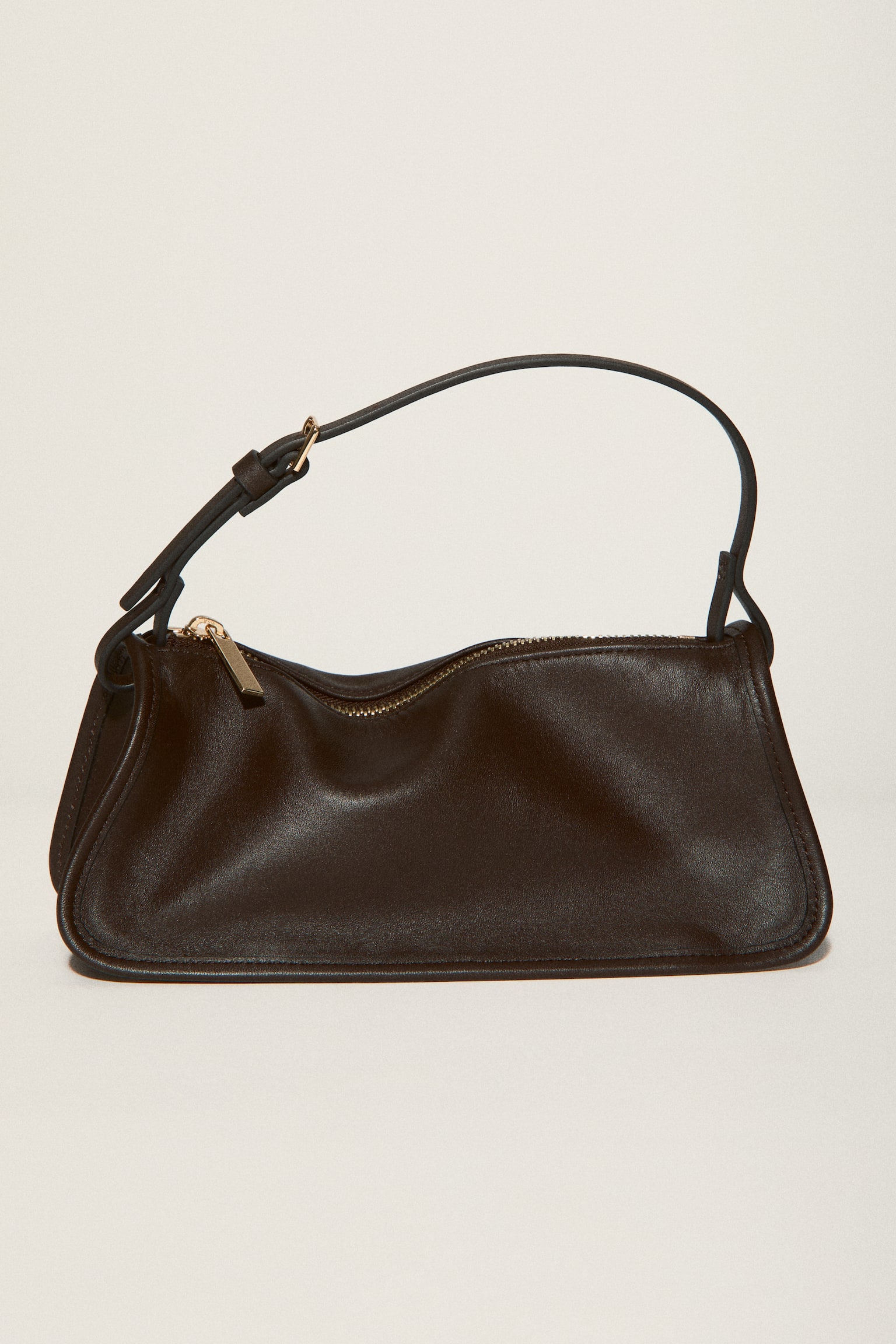 A dark brown smooth leather shoulder bag is displayed from the front, showcasing a rectangular shape with rounded bottom corners. It features a narrow, adjustable shoulder strap with a gold-toned buckle, and a gold-toned zip is visible across the top. - 1