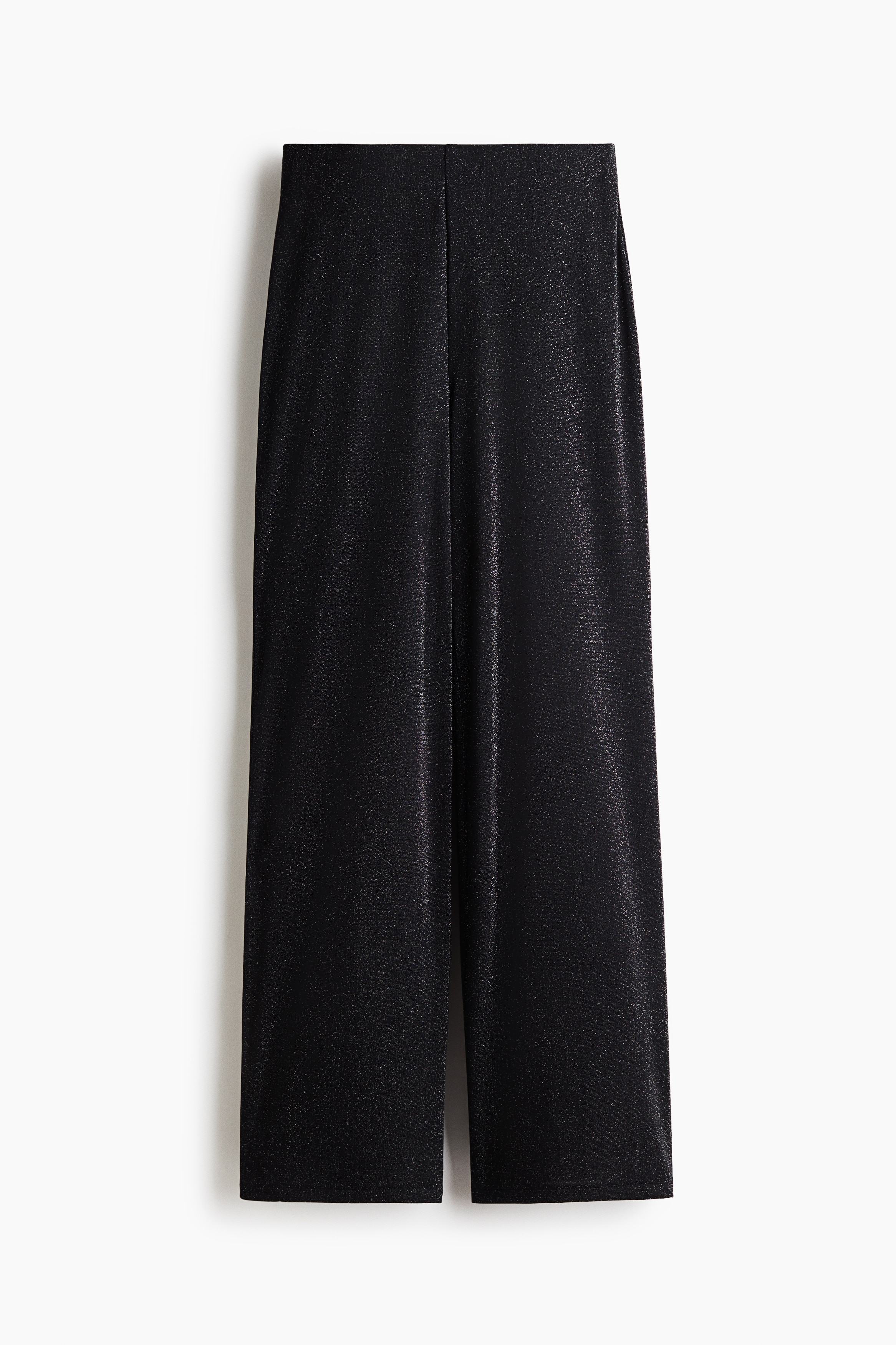 Loose-fit trousers in a shimmering black knit are worn by the model, featuring a high elasticated waist and wide legs. The trousers are styled with a matching loose-fitting, long-sleeved top.
