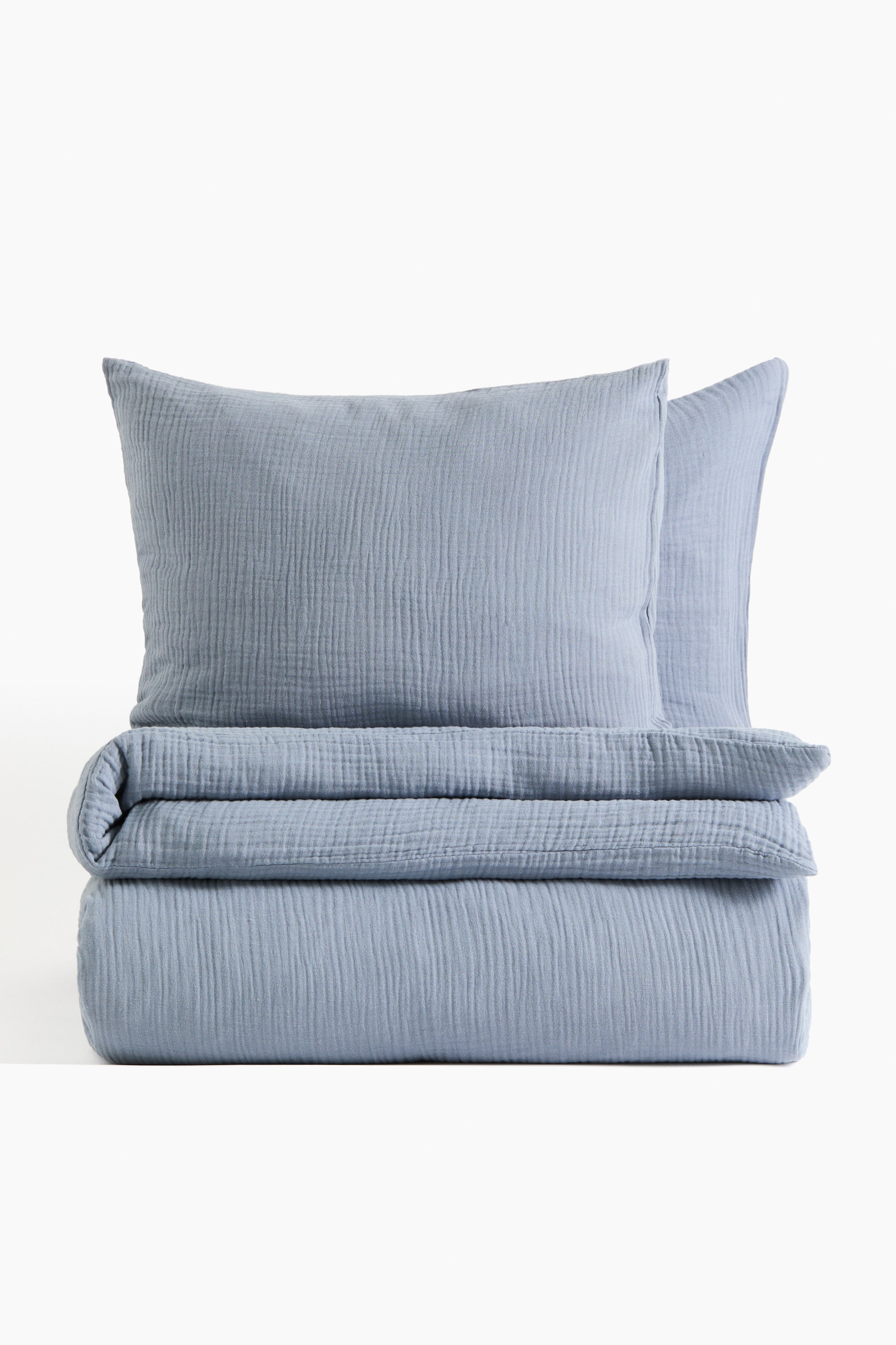 View larger image: A double duvet cover set showcases a folded duvet cover and two pillowcases, all featuring a light blue crinkled cotton muslin texture. The set is arranged front-facing, with one pillowcase resting on the folded duvet cover and another positioned behind it.
