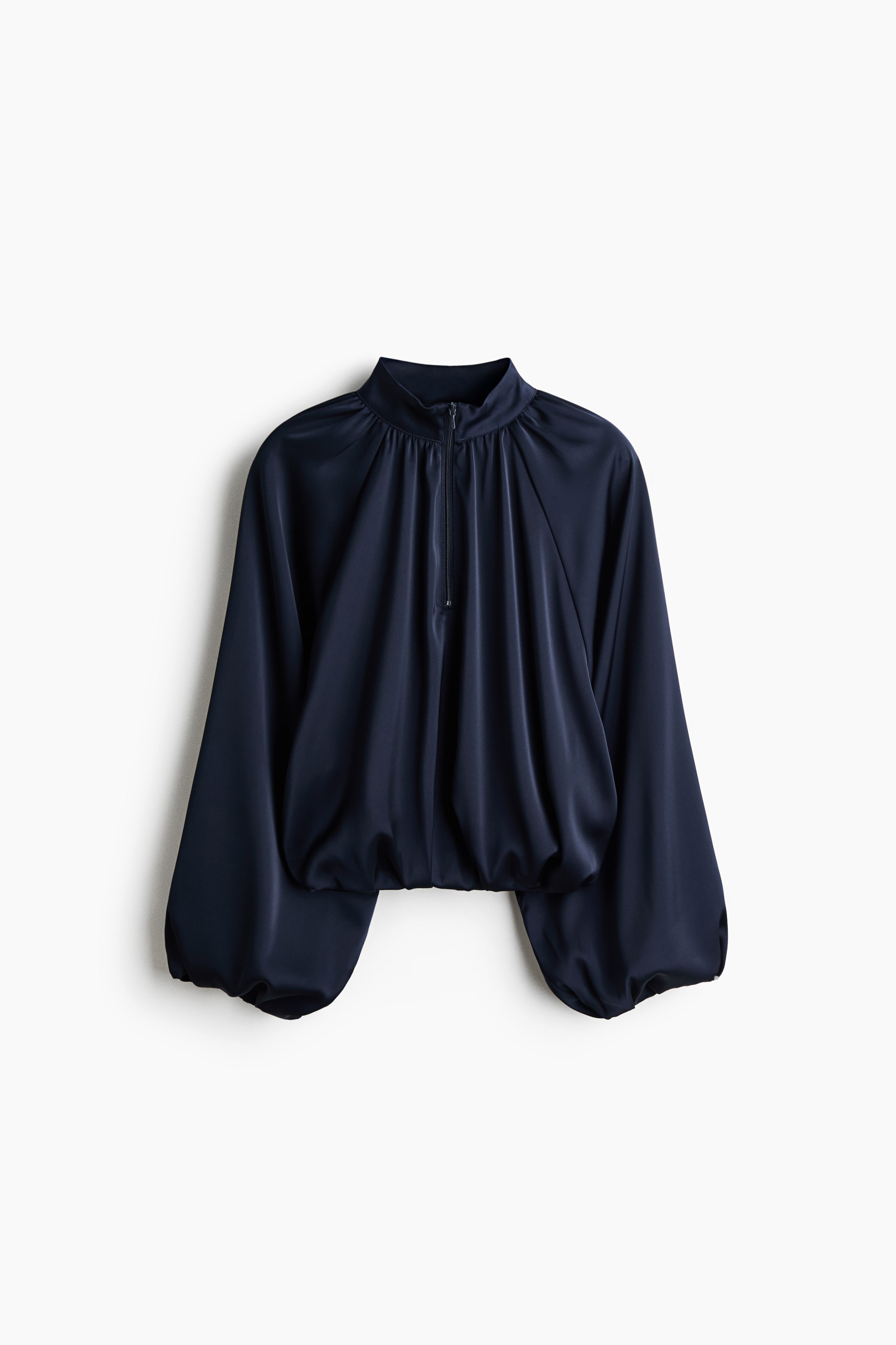 Ampliar la imagen: Una blusa de satén azul marino está orientada hacia el frente, con cuello alto tipo mock neck, cierre frontal con media cremallera y detalles fruncidos que caen sobre el corsé. La prenda presenta mangas globo voluminosas y un dobladillo fruncido que crea una silueta blusón.