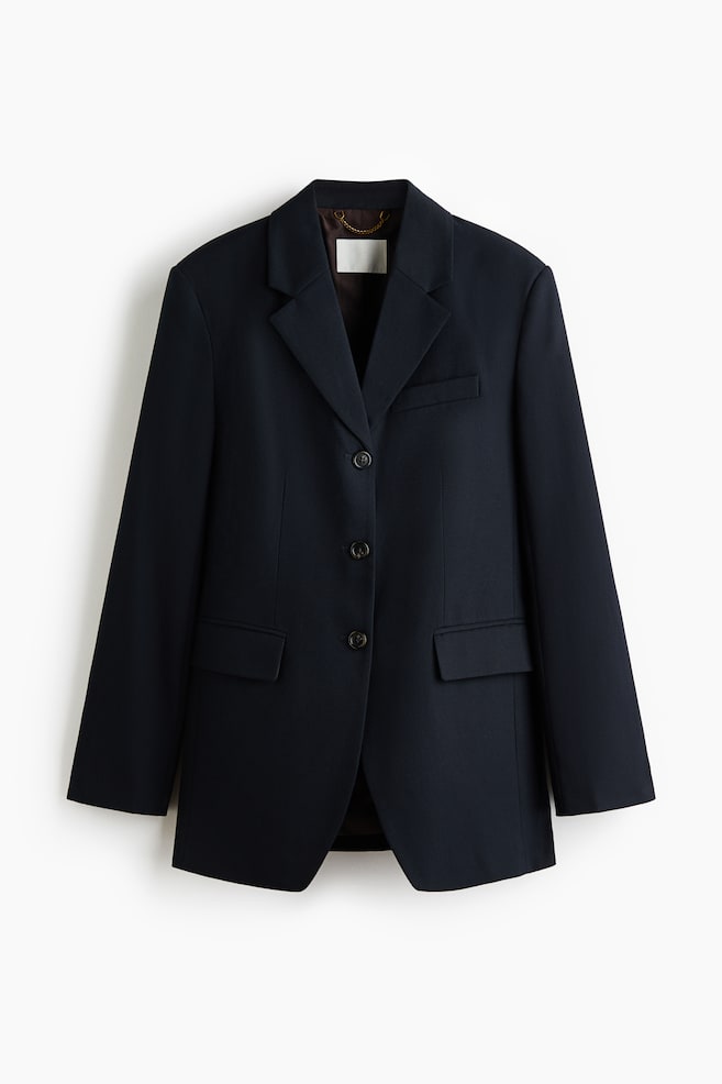 A dark blue blazer is displaying a front view, featuring notch lapels, three dark buttons down the front, and a chest pocket on the left. It is also designed with two flap pockets at the hips, and a brown lining with a small gold-toned chain is visible at the back of the neck. - 1