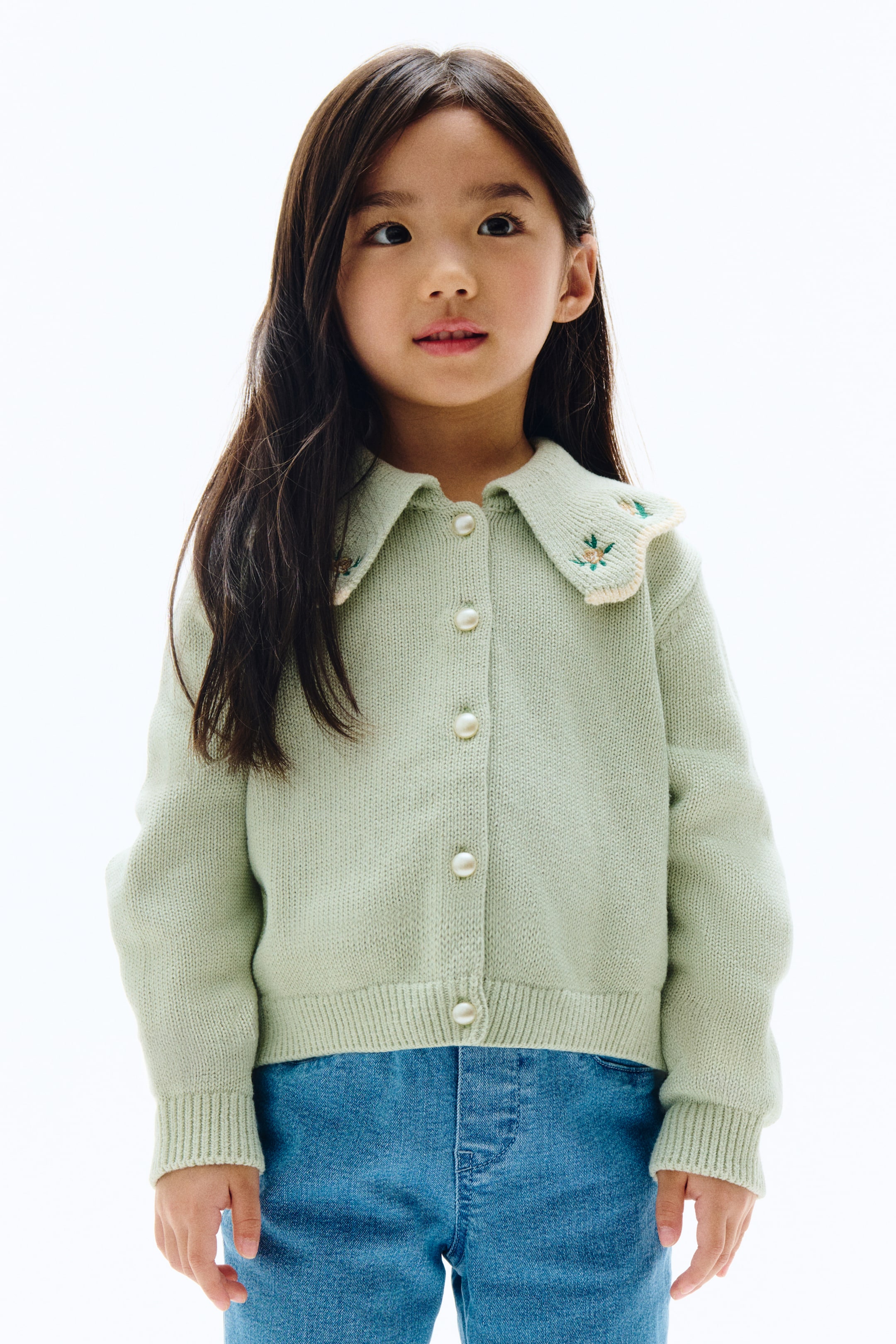 拡大画像を表示: ライトグリーンのニットカーディガンは、小花が刺繍された大きな丸い襟を特徴としており、クリーム色のスカラップエッジで縁取られています。前面はパールのようなボタンで留められており、リブ付きの袖口とリブ付きの裾が特徴です。