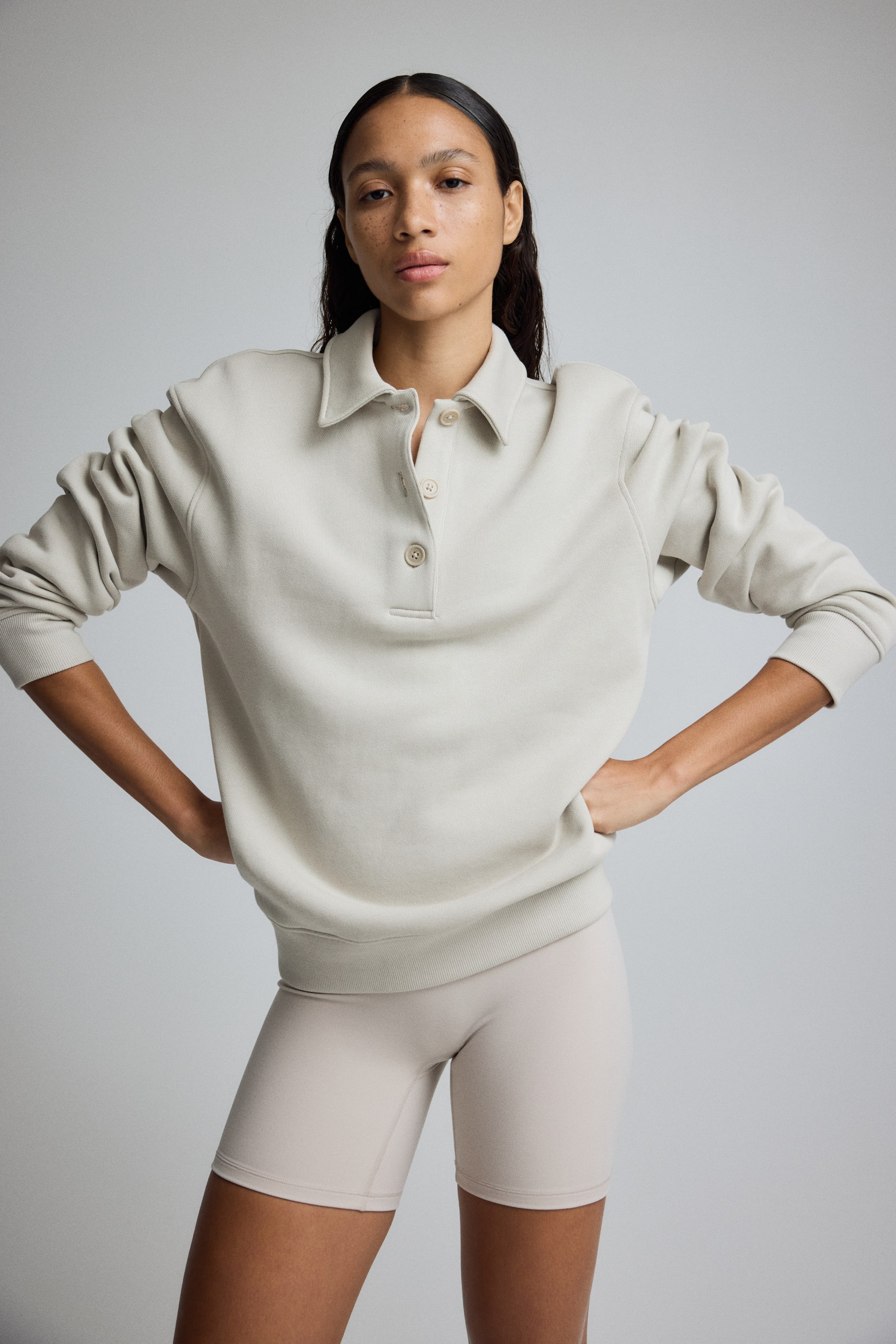 Grotere afbeelding bekijken: Een lichtbeige sweatshirt verschijnt aan de voorkant, met een puntige kraag en een placket met drie knopen in lichte kleuren. Het is ontworpen met lange mouwen, geribde boorden en een geribde zoom.