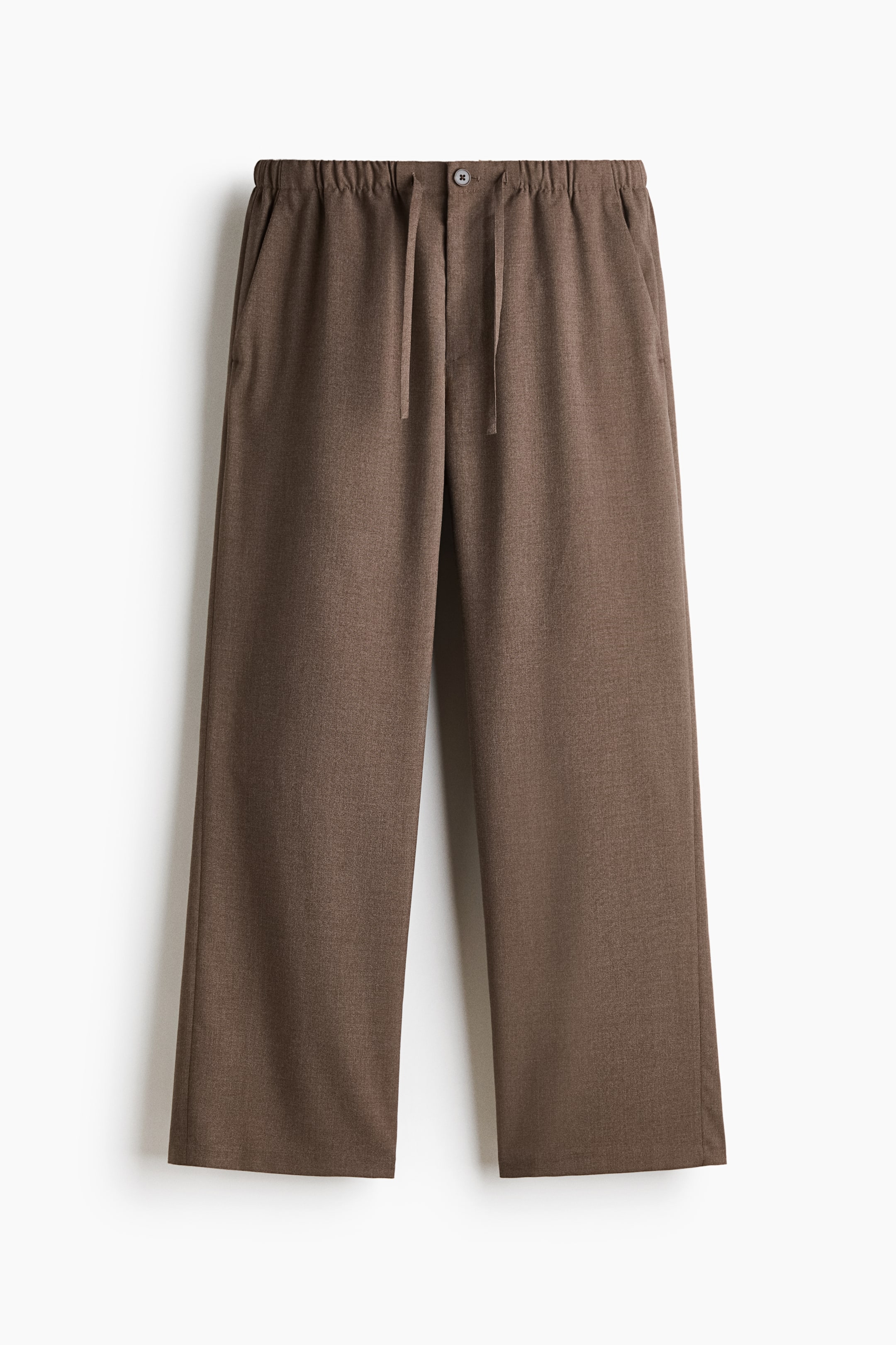 View larger image: A pair of brown textured trousers is shown from the front, featuring an elasticated waistband with a central button closure and matching drawstrings. The trousers have a relaxed, straight-leg silhouette and include side slip pockets.