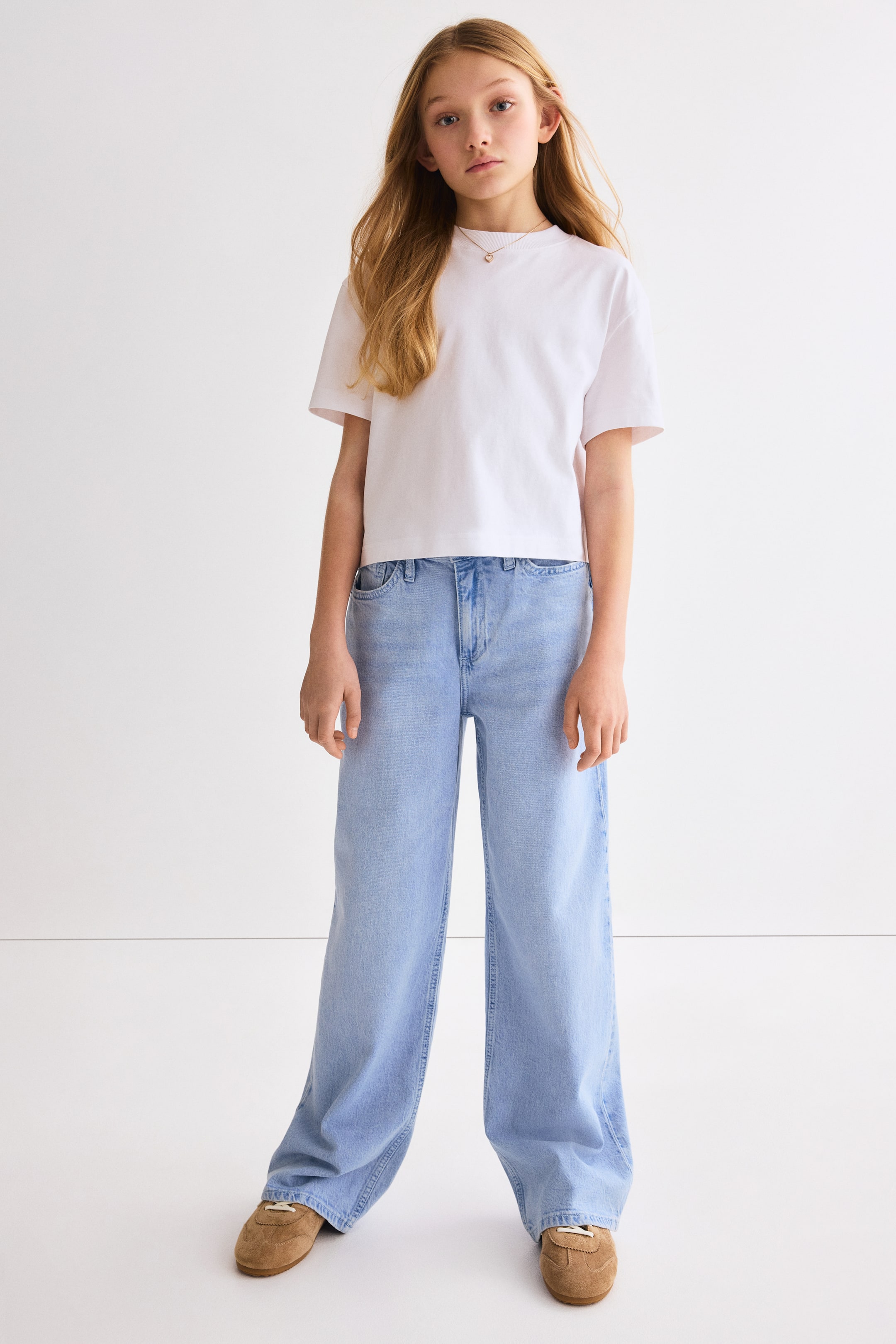 Grösseres Bild ansehen: Hellblaue Jeans mit weitem Bein werden präsentiert, nach vorne gerichtet. Sie zeichnen sich durch eine hochgeschnittene Taille und eine lockere Passform am Bein aus, wobei die Säume die Schuhoberteile bedecken.