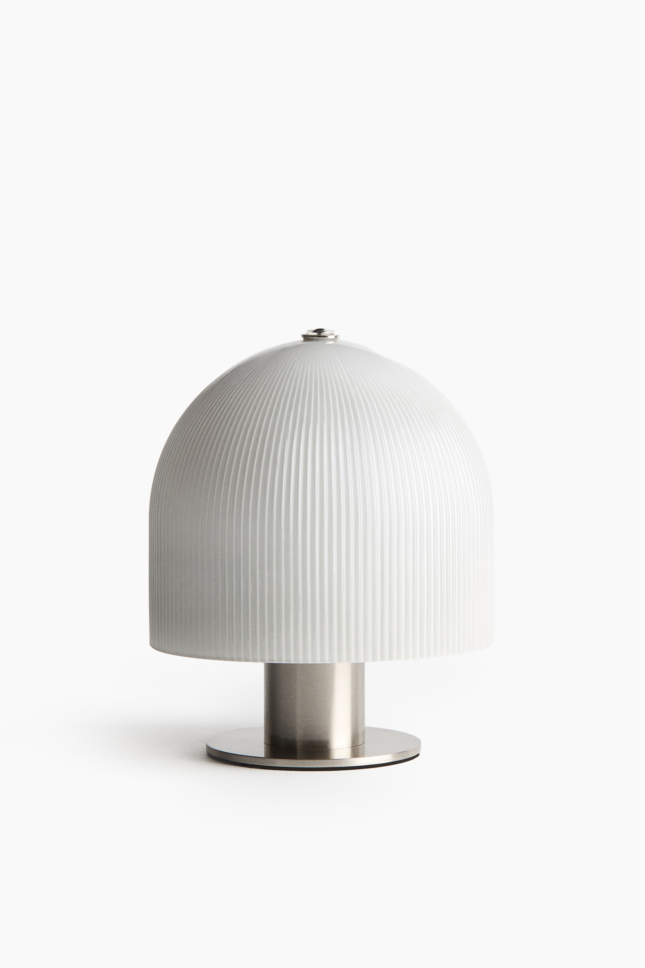View larger image: A table lamp is positioned facing forwards, featuring a dome-shaped, white glass shade with fine vertical ribbing. The shade rests on a short, cylindrical stem made of brushed metal, which is supported by a flat circular base.