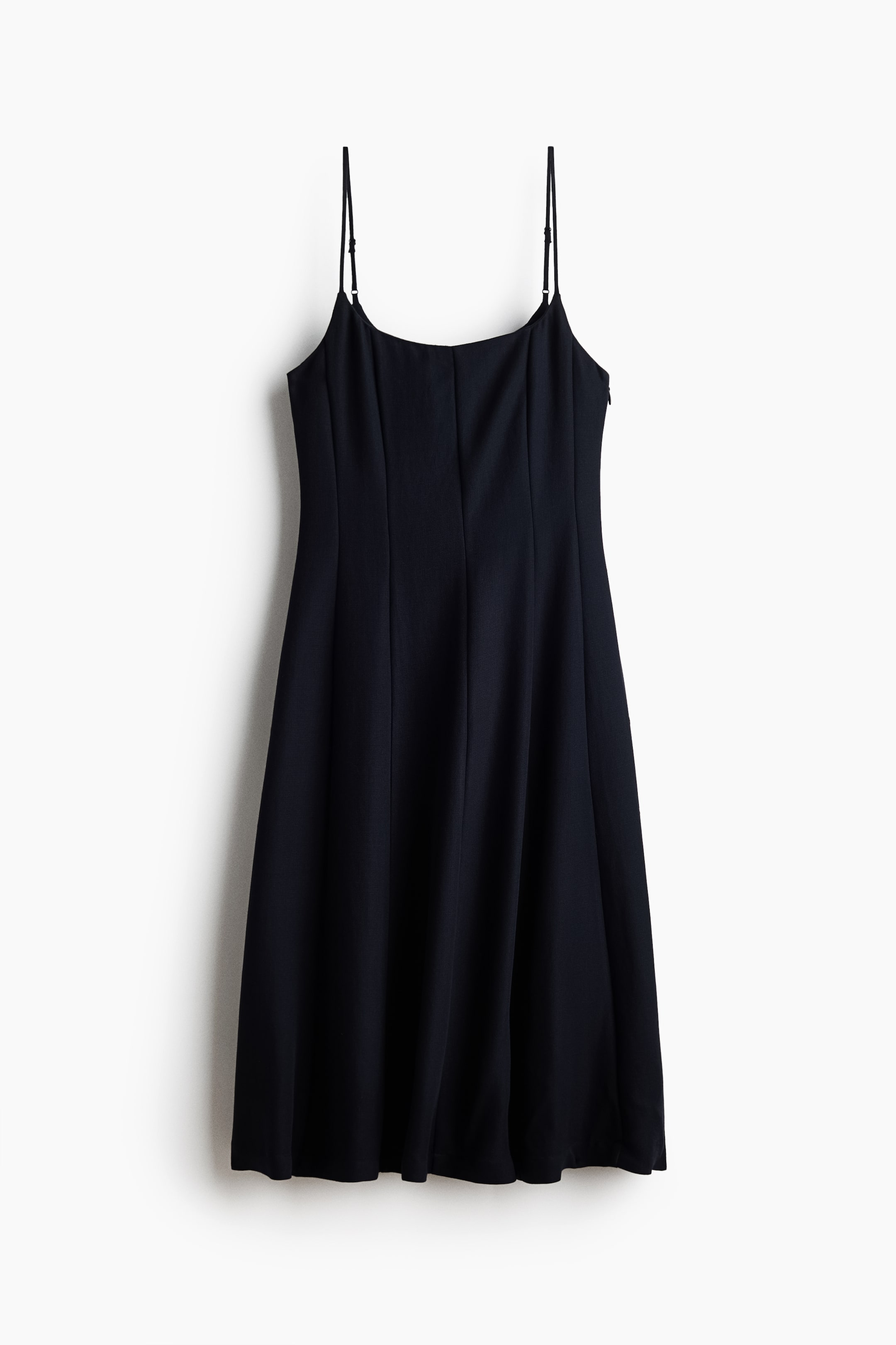 View larger image: A black slip dress features a straight neckline, thin adjustable spaghetti straps, and a fitted bodice with vertical seams. It flows into a subtly flared A-line skirt, with a concealed zipper visible on the right side.