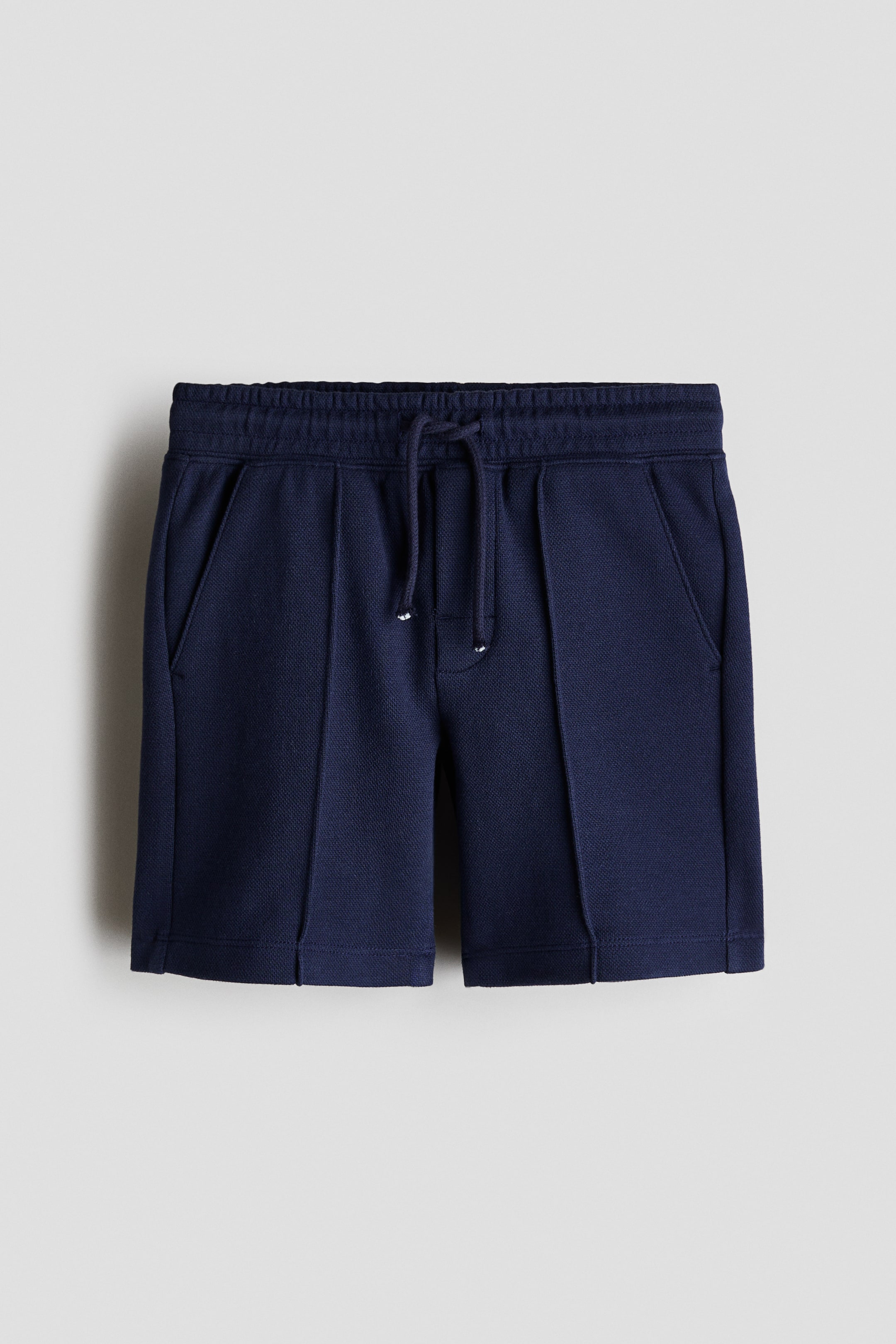 View larger image: Navy blue shorts are shown facing forward, showcasing a subtle knit texture. They feature an elastic waistband, a tied drawstring with white aglets, two side slash pockets, and vertical stitched seams running down the front of each leg.