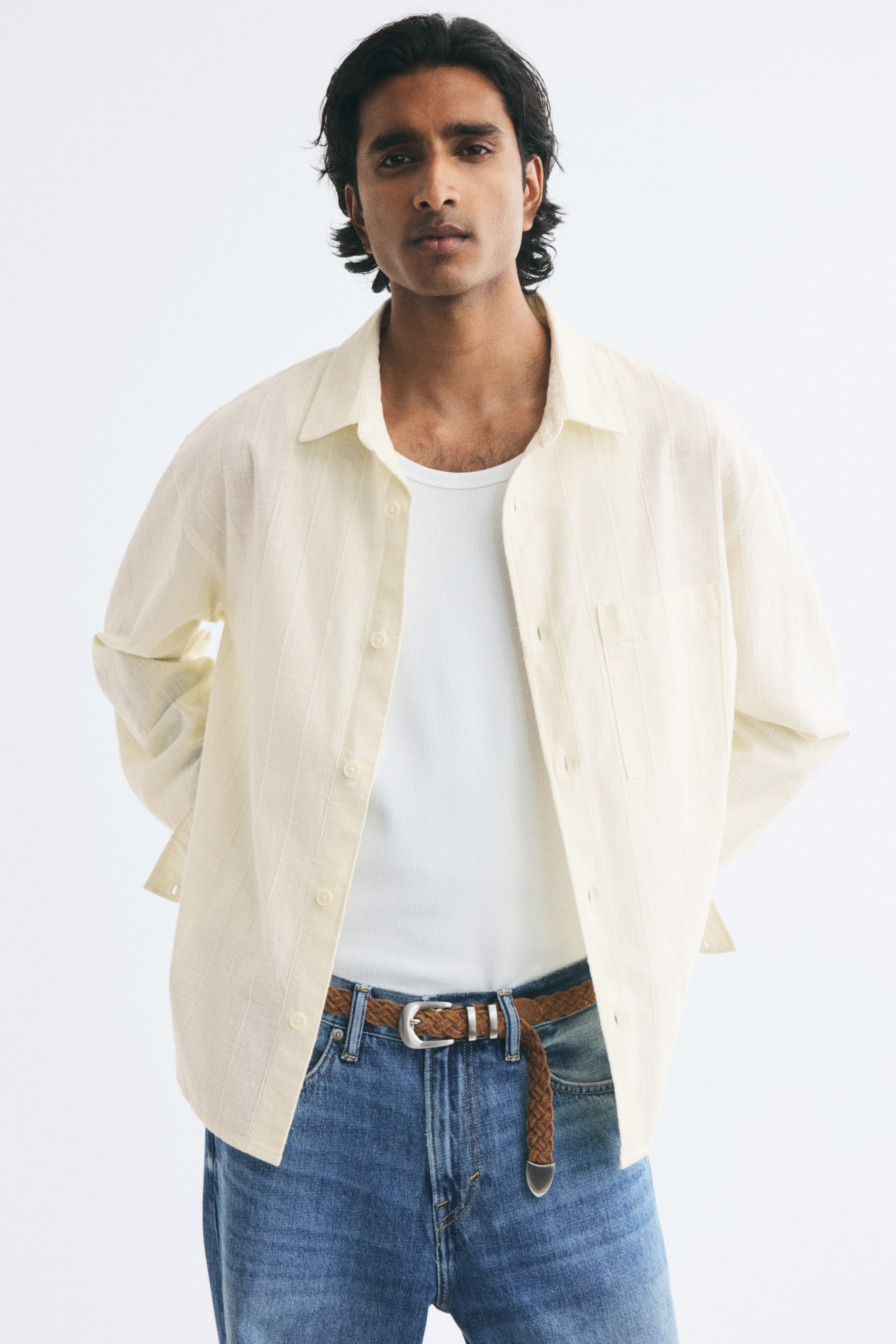 View larger image: A cream-coloured, long-sleeved shirt in a textured cotton dobby weave is worn open over a white ribbed tank top and blue jeans by the model. The relaxed-fit shirt features a collar, a French front, and a single open chest pocket on the left.