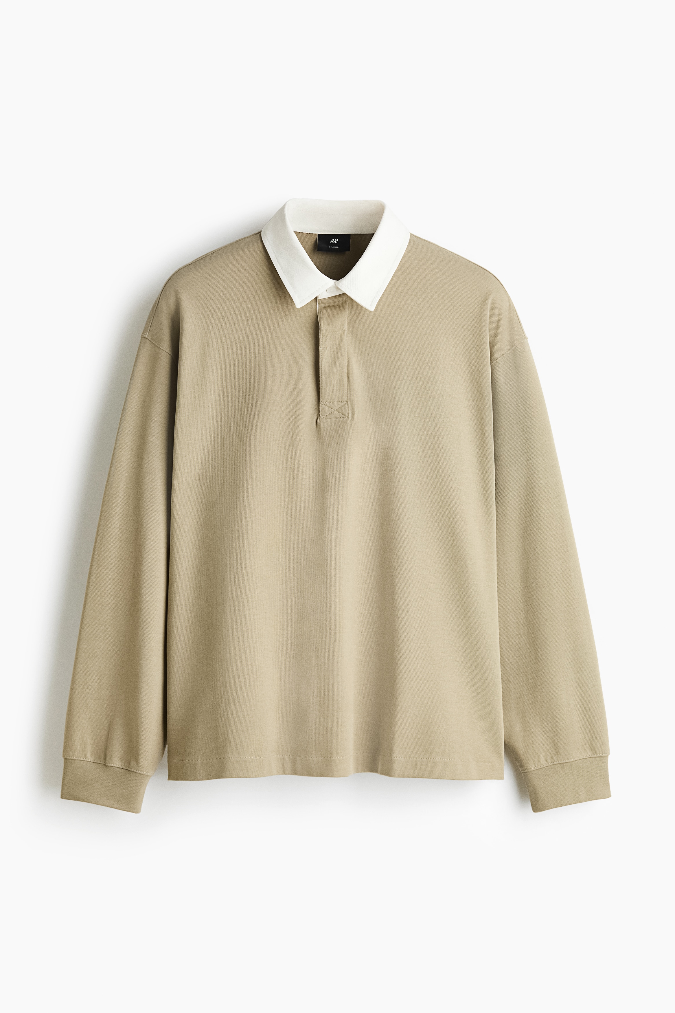 A beige cotton-jersey rugby shirt with a contrasting white collar and a concealed button placket is worn by the model. The shirt features a relaxed fit with dropped shoulders and ribbed cuffs, and is paired with dark wide-leg jeans.