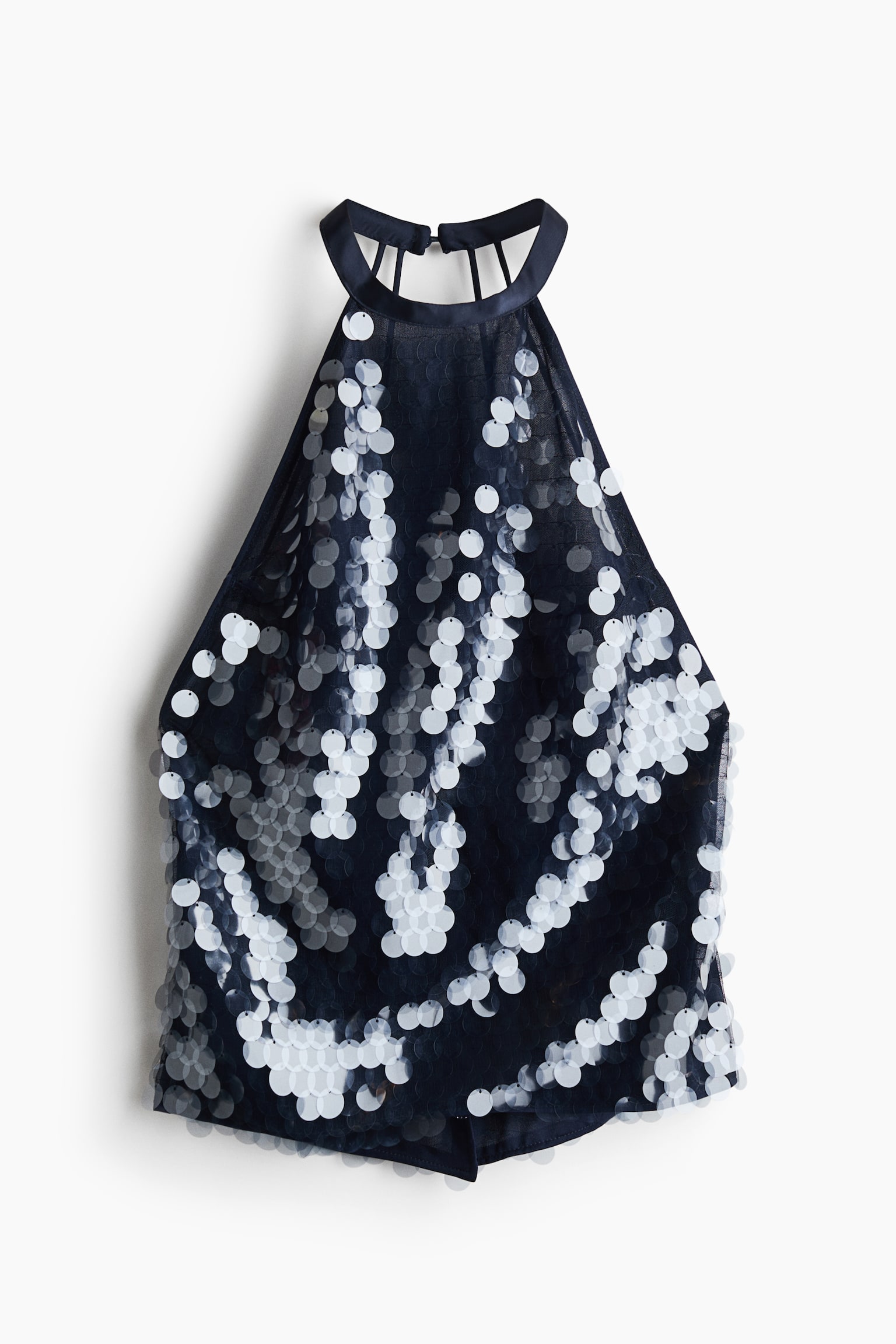 A navy blue halter top is shown from the front, highlighting a sheer fabric embellished with large, round, white and silver-toned paillettes arranged in wavy vertical patterns. The top features a high halter neckline with a solid band and thin vertical straps visible at the back.