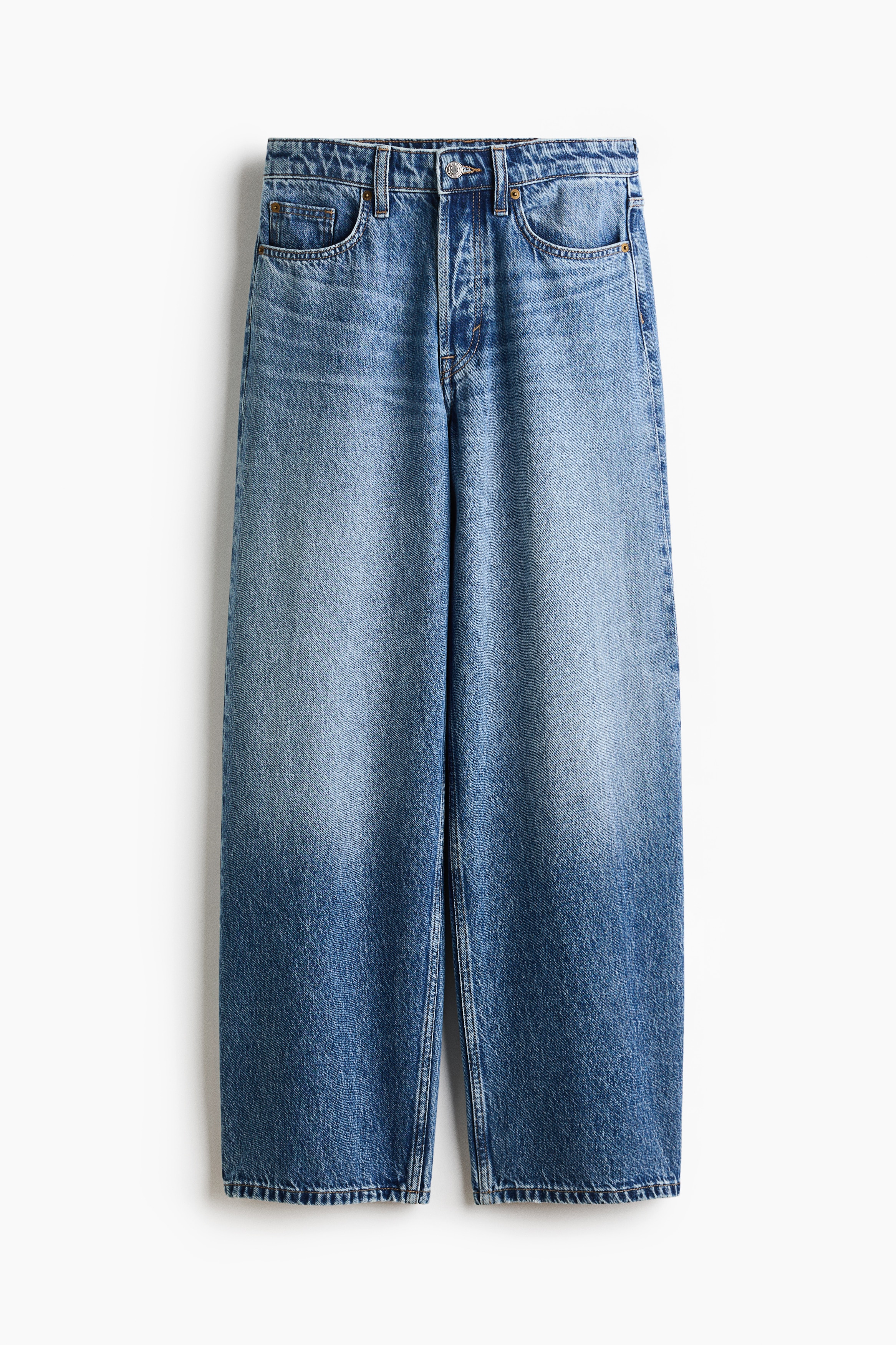 LyseblÃ¥ vasket denimjeans med avslappet passform bÃ¦res av modellen i en hukende posisjon. Jeansen er stylet med en mÃ¸rk marineblÃ¥ langermet poloskjorte og svarte flate sko.