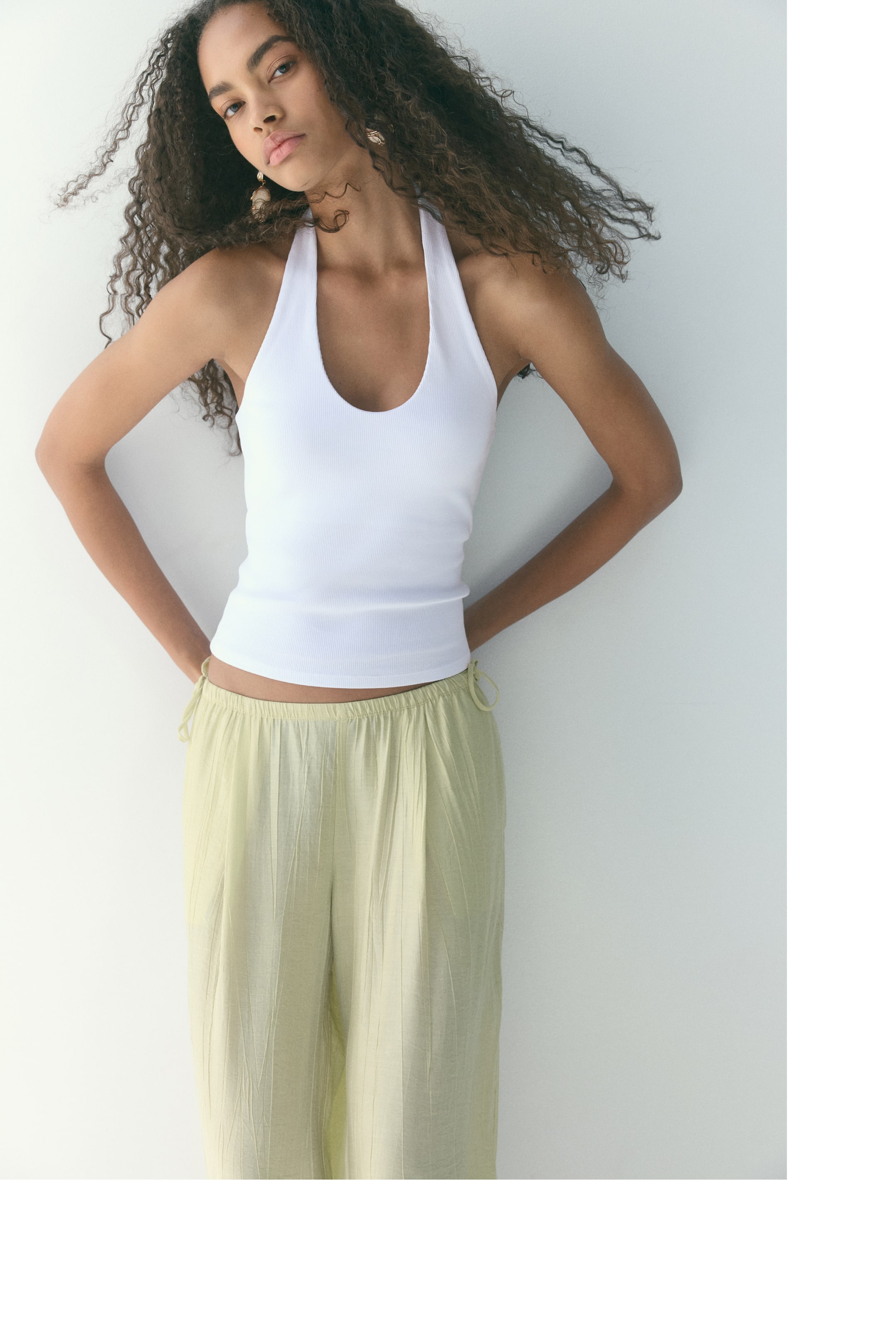 View larger image: The model is wearing a short halterneck top crafted from ribbed cotton jersey. It boasts a slim fit, a scoop neckline, and a straight-cut hem, styled over light green trousers.