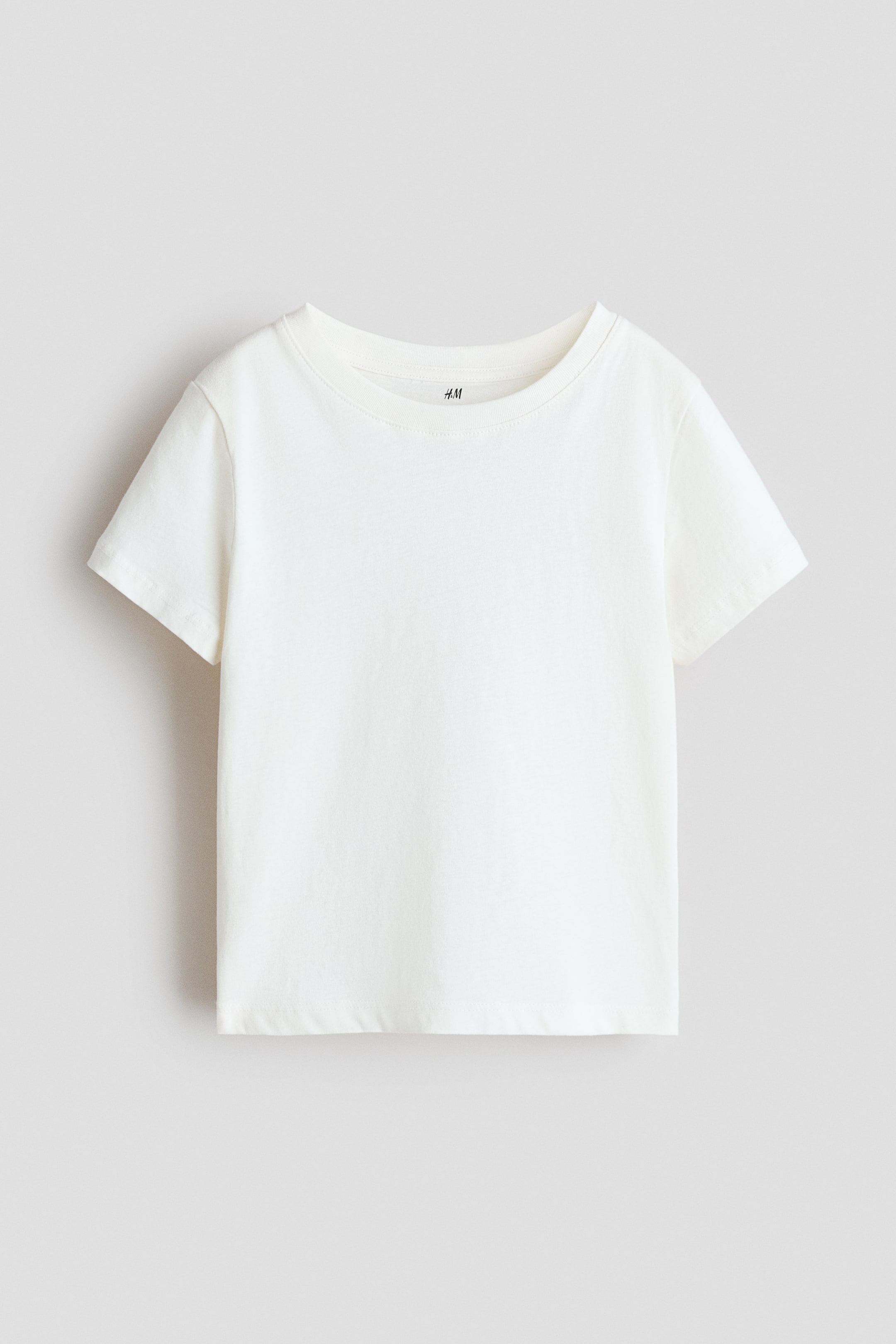 Xem ảnh lớn hơn: Một chiếc áo phông trắng đang quay MẶT TRƯỚC, thể hiện bề mặt vải mịn, cổ tròn xếp nếp và tay ngắn.