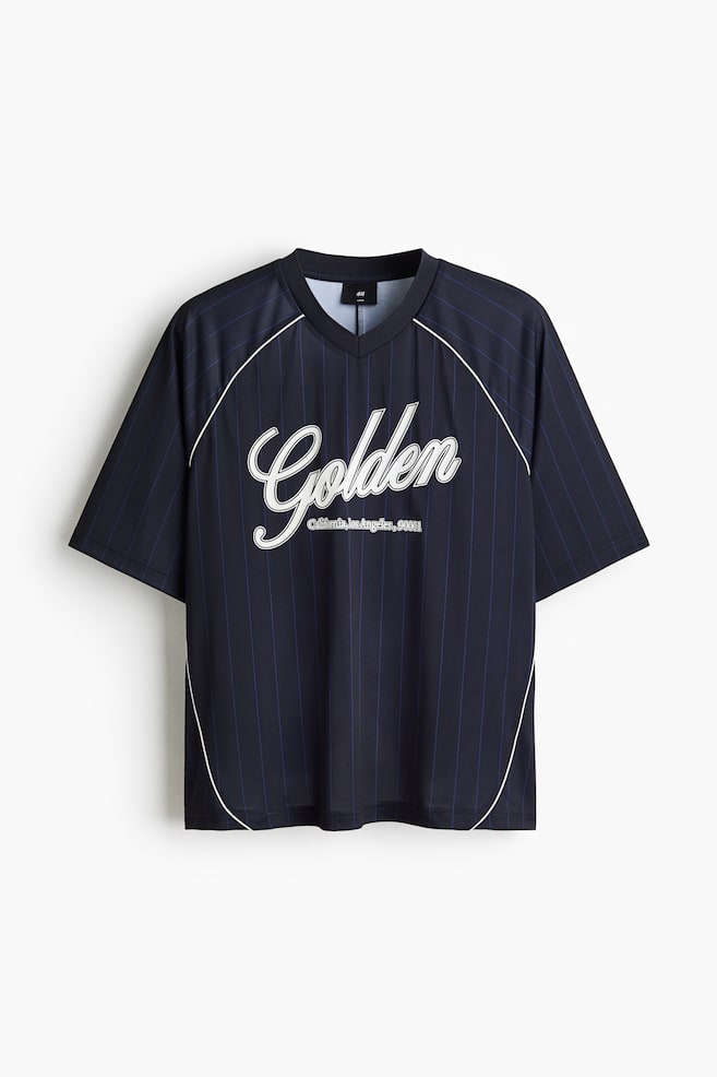 Ein Jersey-T-Shirt wird von vorne gezeigt, mit einer dunkelblauen Basis und dünnen vertikalen blauen Nadelstreifen sowie einem weißen "Golden"-Schriftzug auf der Brust, darunter "California, Los Angeles, 90001". Es ist mit einem gerippten V-Ausschnitt, kurzen Raglanärmeln und einem geraden Saum gestaltet, mit schmalen weißen Paspeln, die die Raglannähte und Seiten nachzeichnen, und präsentiert einen lockeren Sitz. - 1