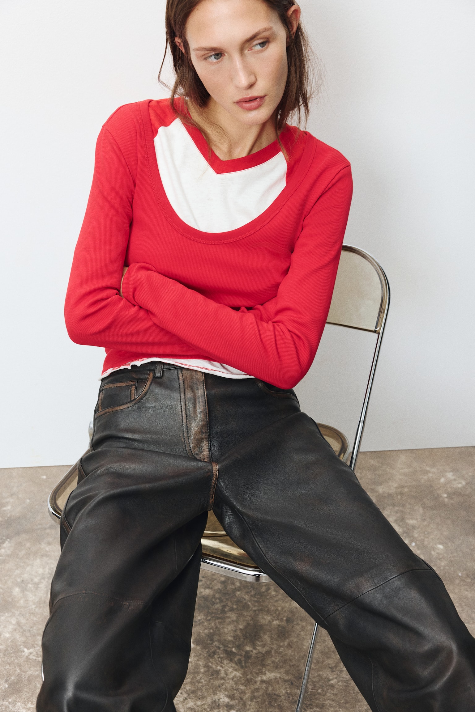 A pair of dark brown leather trousers is hanging front-facing, featuring a high-waisted fit with belt loops and a classic five-pocket construction. The trousers feature a distressed, burnished finish along the seams and edges, highlighted by horizontal knee seams and vertical side seams. - 1