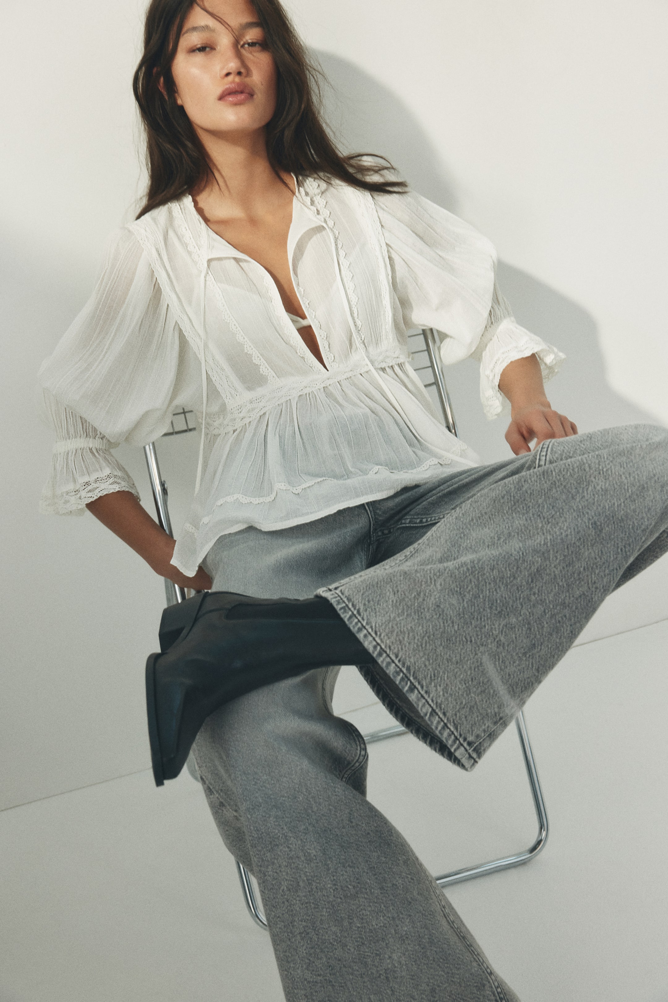 View larger image: A white blouse is showcasing a deep V-neckline with lace trim and a tie closure, revealing a white bralette underneath. It features puffed long sleeves with ruffled lace cuffs and an empire waistline from which the fabric is gathered, creating a flowing silhouette.