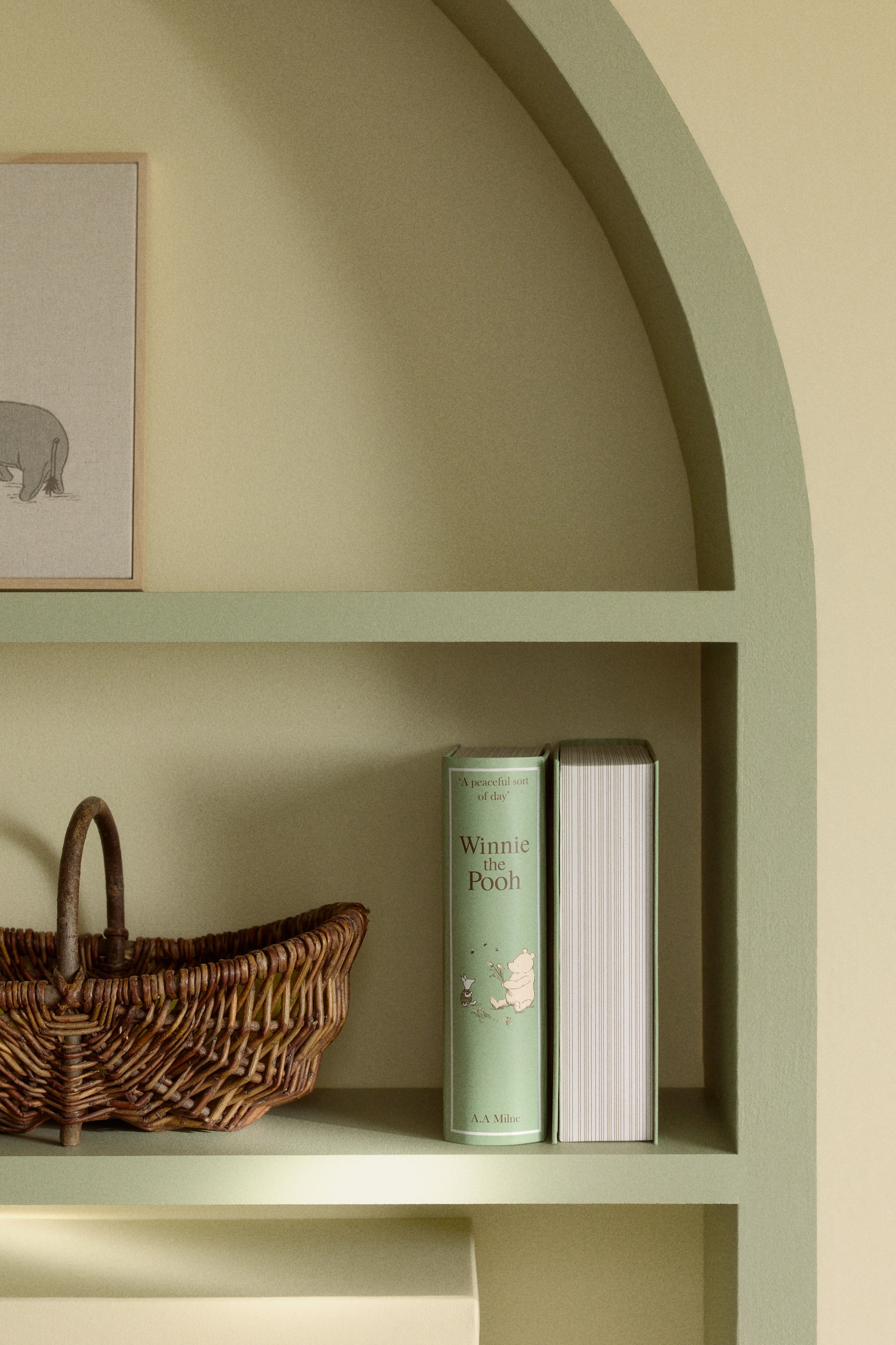 View larger image: Two books are standing upright. The book on the left showcases a light green cover featuring an illustration of Winnie the Pooh and Piglet, titled 'Winnie the Pooh'. The second book is positioned to its right, revealing its white pages with faint horizontal lines.