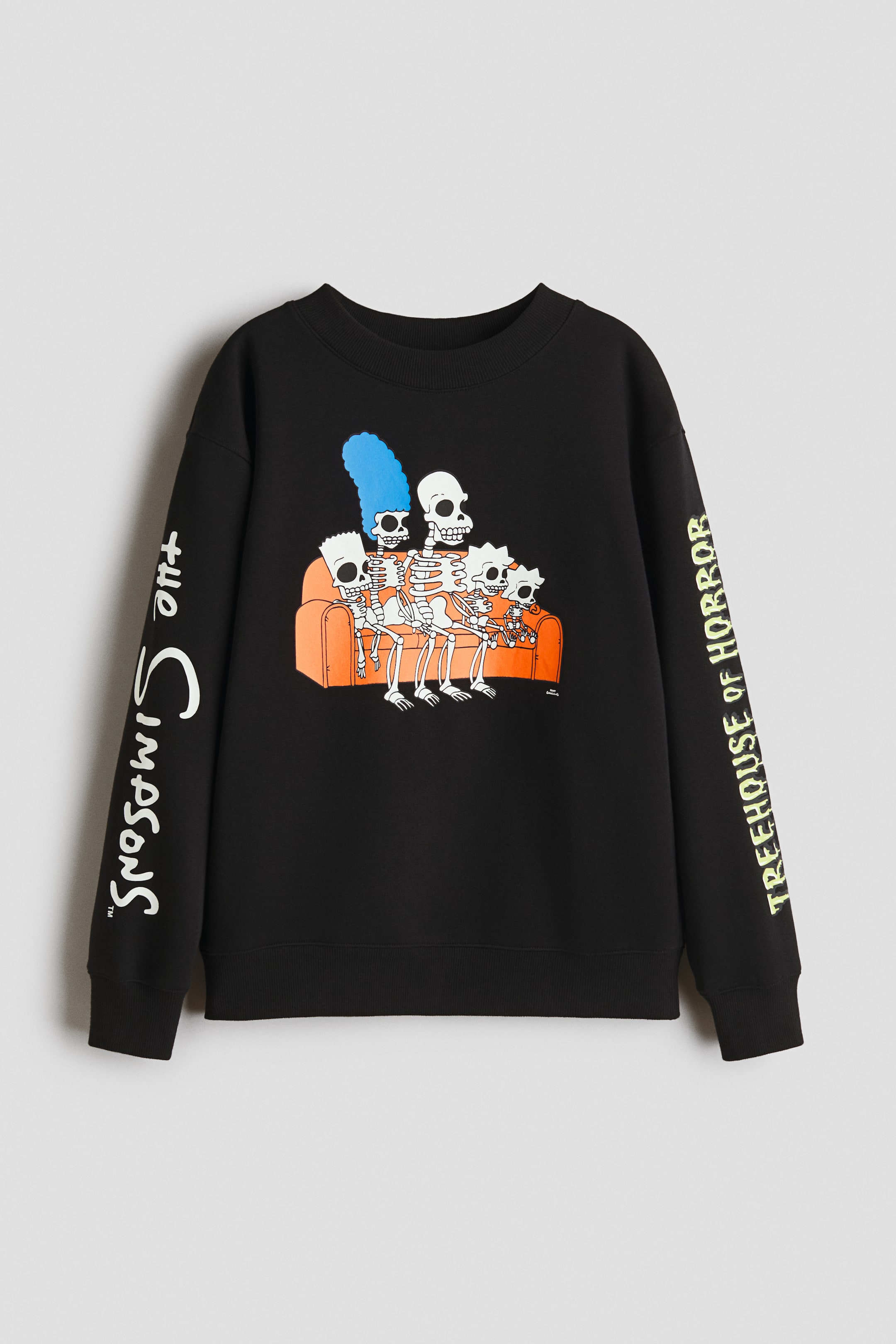 View larger image: A black relaxed-fit sweatshirt is shown from the front, featuring a print of The Simpsons family depicted as skeletons sitting on an orange sofa. It is designed with a round, rib-trimmed neckline, dropped shoulders, long sleeves with ribbed cuffs, and a ribbed hem, while displaying vertical white text 'the Simpsons?' on the left sleeve and vertical yellow text 'TREEHOUSE OF HORROR' on the right sleeve.