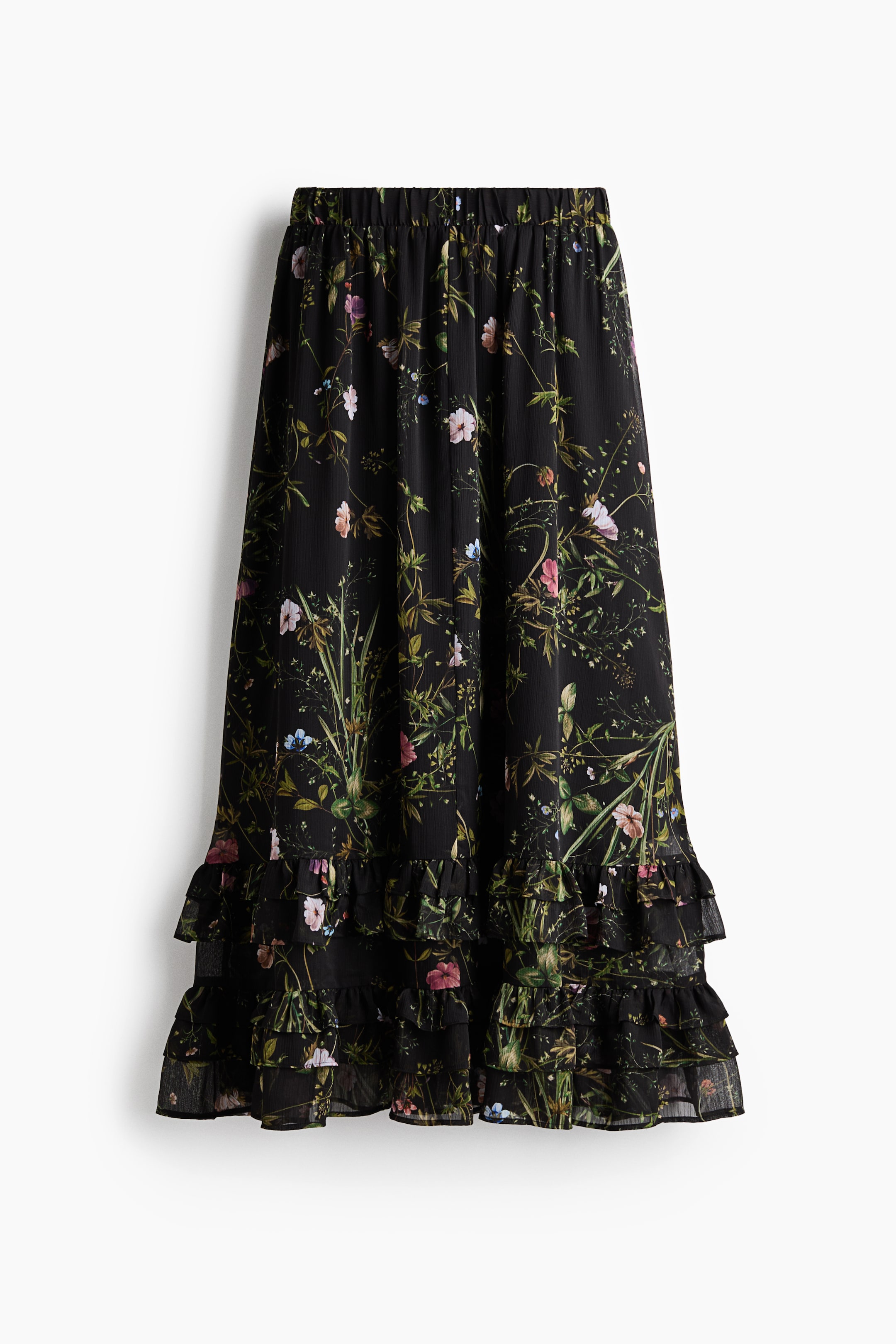 View larger image: A black floral-print skirt is hanging in a front-facing view, displaying a gathered elastic waistband and a flowing silhouette with a botanical wildflower pattern. The lightweight fabric drapes down to a double-tiered ruffled hem.