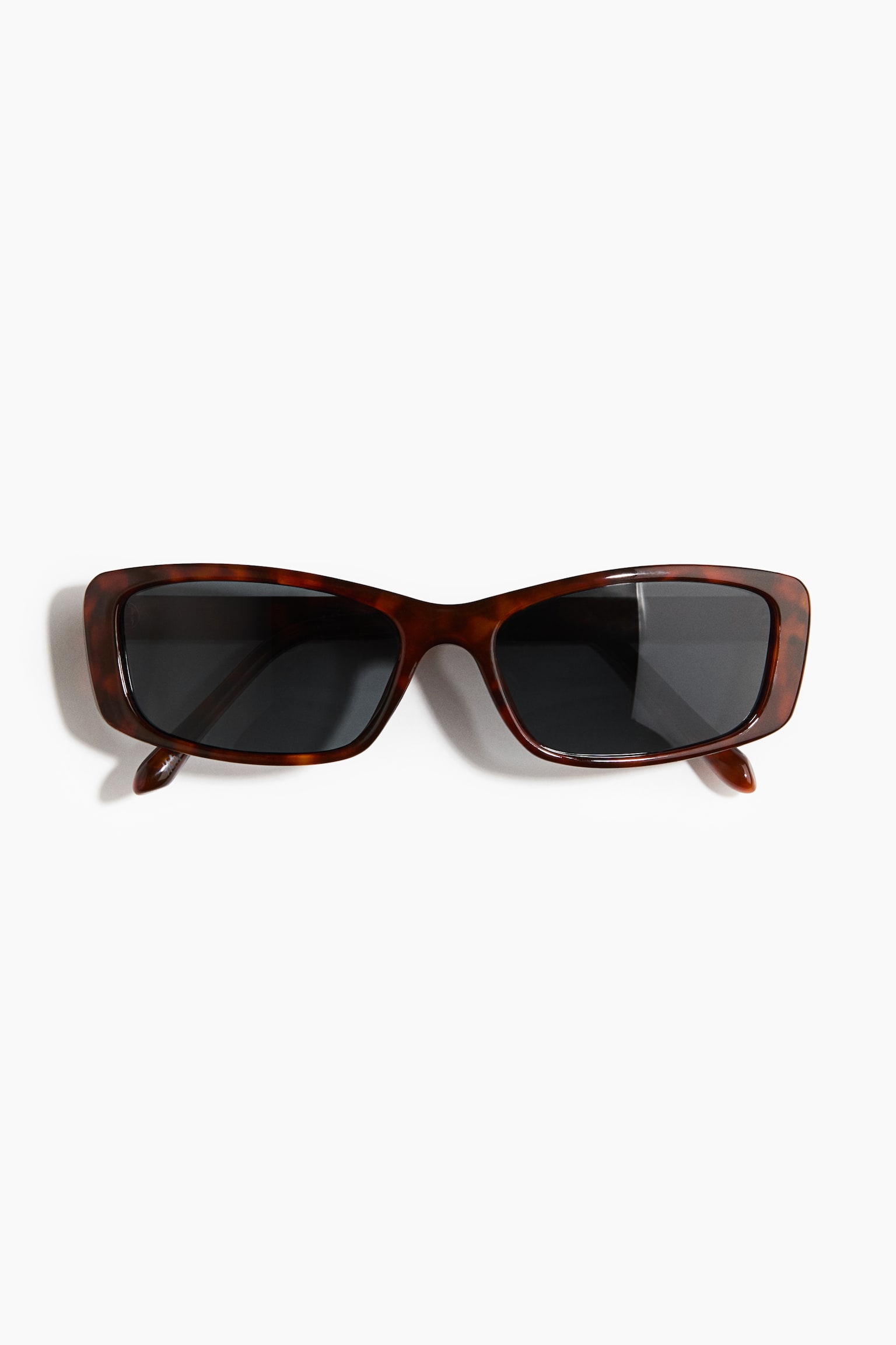 Unos lentes de sol cuadrados con armazón de plástico con estampado carey y lentes oscuros reposan extendidos, de frente, para mostrar su forma rectangular y sus varillas plegadas.