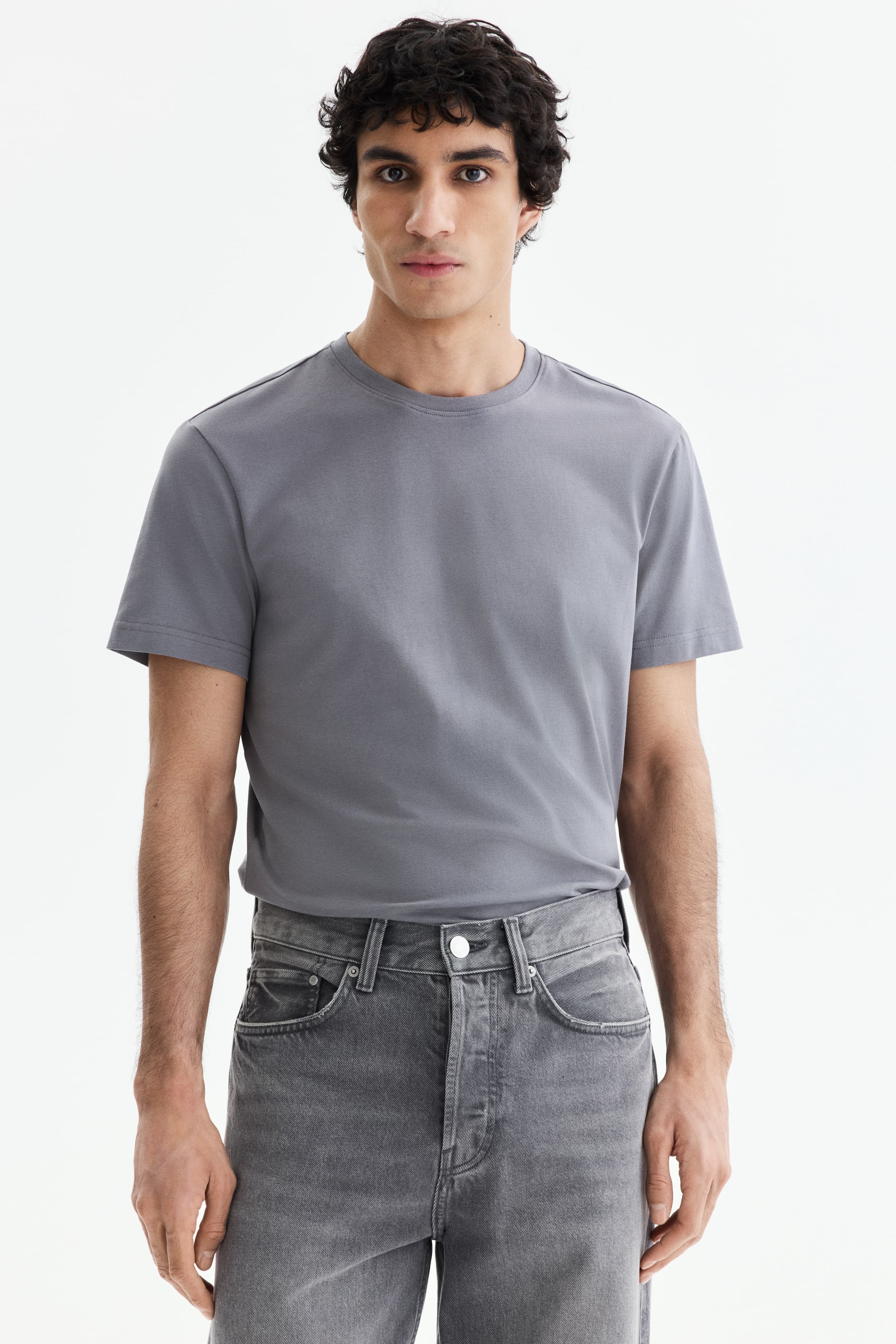Προβολή μεγαλύτερης εικόνας: Γκρι μπλουζάκι με στρογγυλή λαιμόκοψη, κοντά μανίκια και λεία υφή, που εφαρμόζει κανονικά και είναι φορεμένο μέσα από γκρι τζιν.
