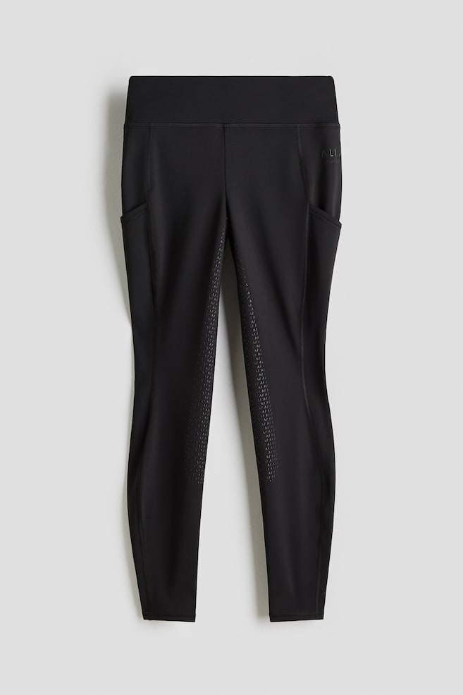 Black riding tights are presenting from the front, featuring a wide waistband, side pockets on both legs with a subtle logo on the right pocket, and a silicone grip pattern on the inner legs. - 1