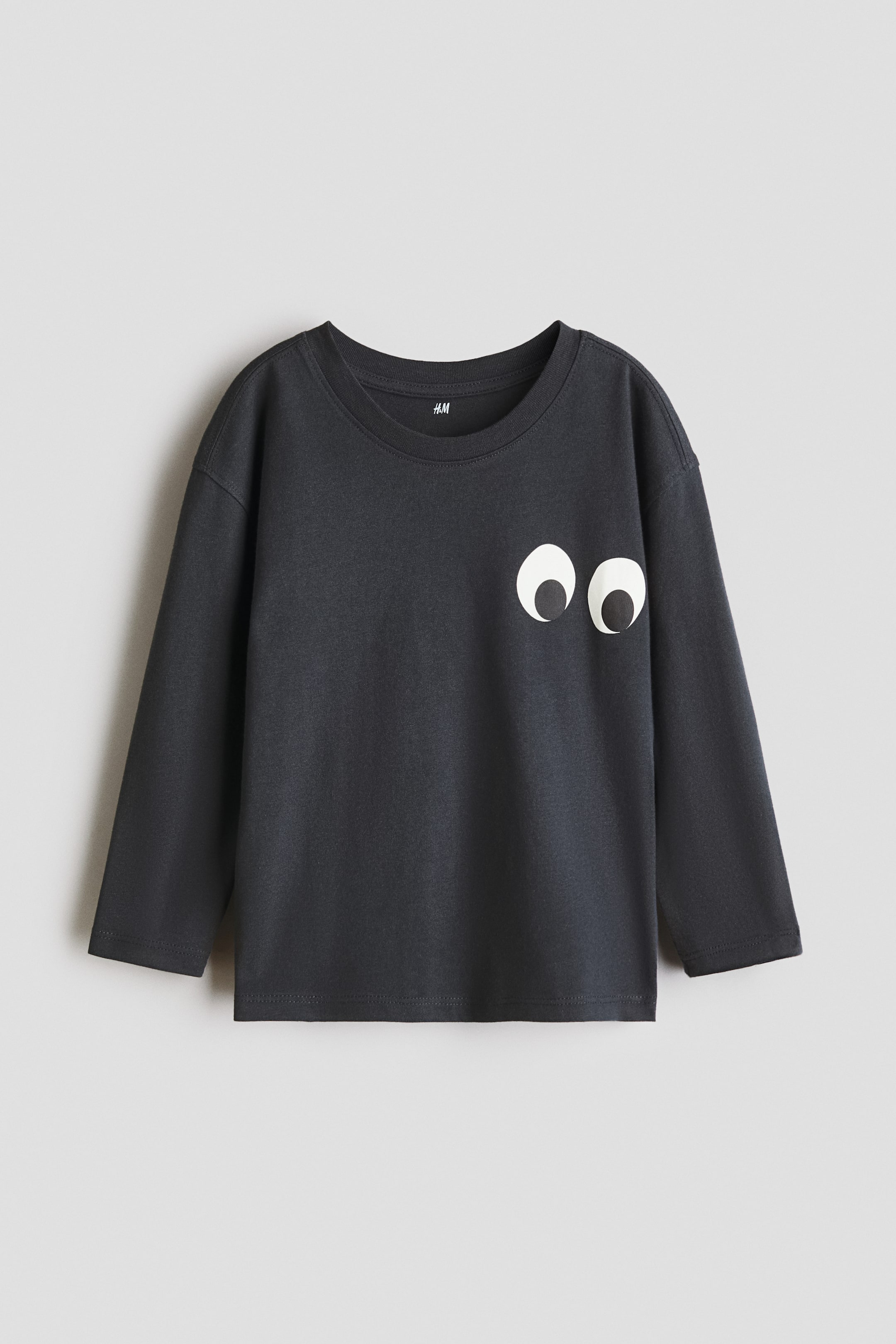 View larger image: A dark gray long-sleeved t-shirt in cotton jersey featuring a round, trimmed neckline and dropped shoulders, displaying two white cartoon eyes with black pupils printed on the front.