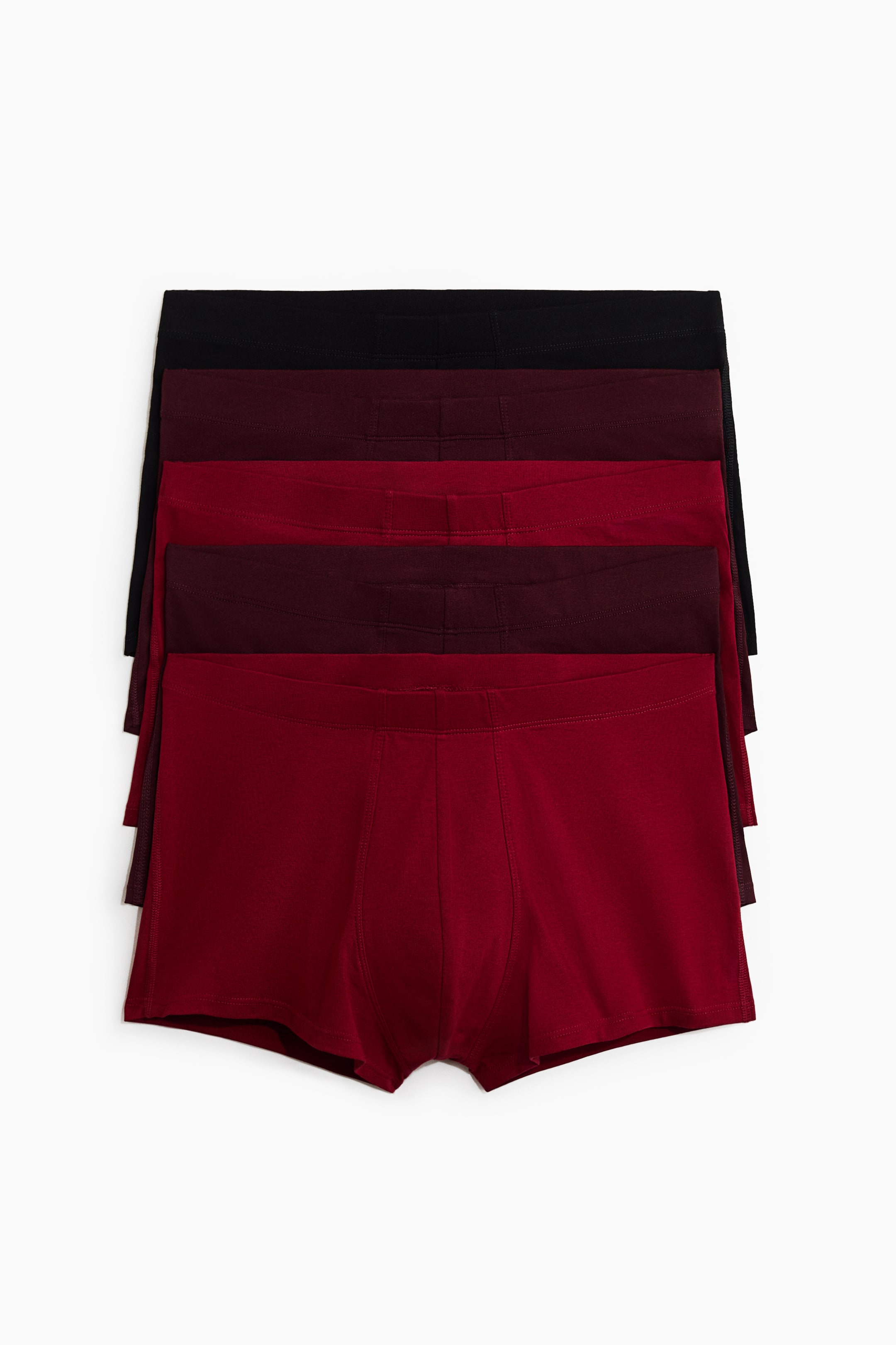 Größeres Bild ansehen: Ein Fünferpack Herren-Trunks wird in einer frontalen Ansicht mit fünf Paaren gezeigt, die vertikal gestapelt sind. Der Stapel zeigt Farben von Schwarz bis Dunkelburgunderrot und Rot, wobei jedes Paar einen bedeckten elastischen Bund, Flatlock-Nähte an einer gefütterten Fronttasche und kurze Beine aufweist.