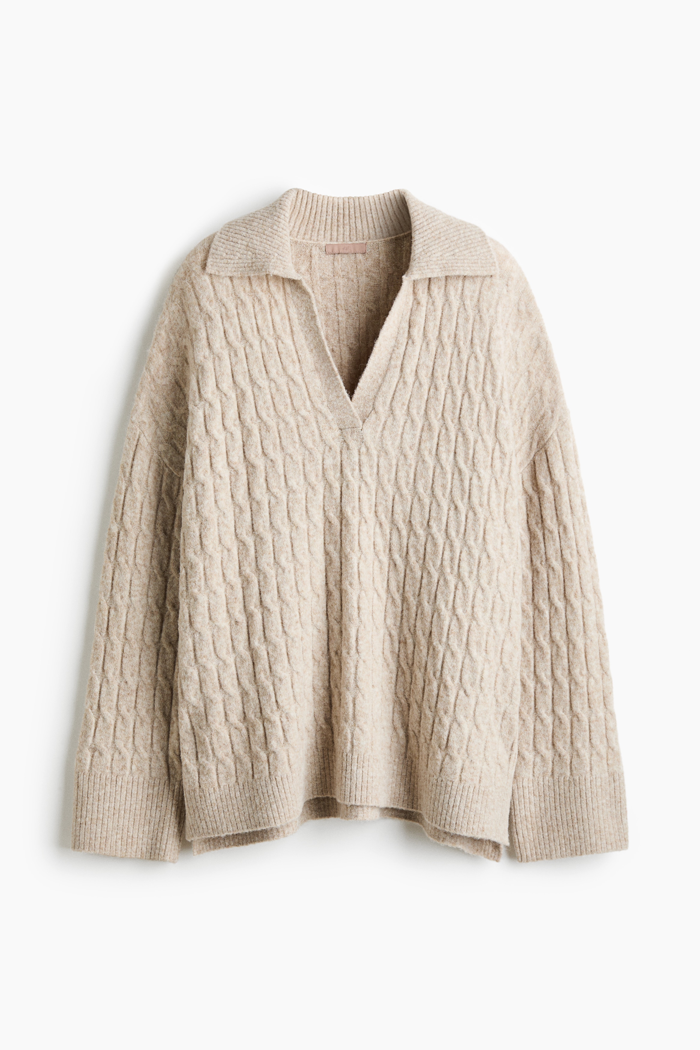 Un pull beige en maille torsadÃ©e est prÃ©sentÃ© de face, avec une coupe dÃ©contractÃ©e, un col polo ouvert et un dÃ©colletÃ© en V. Le pull affiche une texture torsadÃ©e sur lâensemble, des Ã©paules tombantes et des finitions cÃ´telÃ©es, portÃ© sur un pantalon blanc.