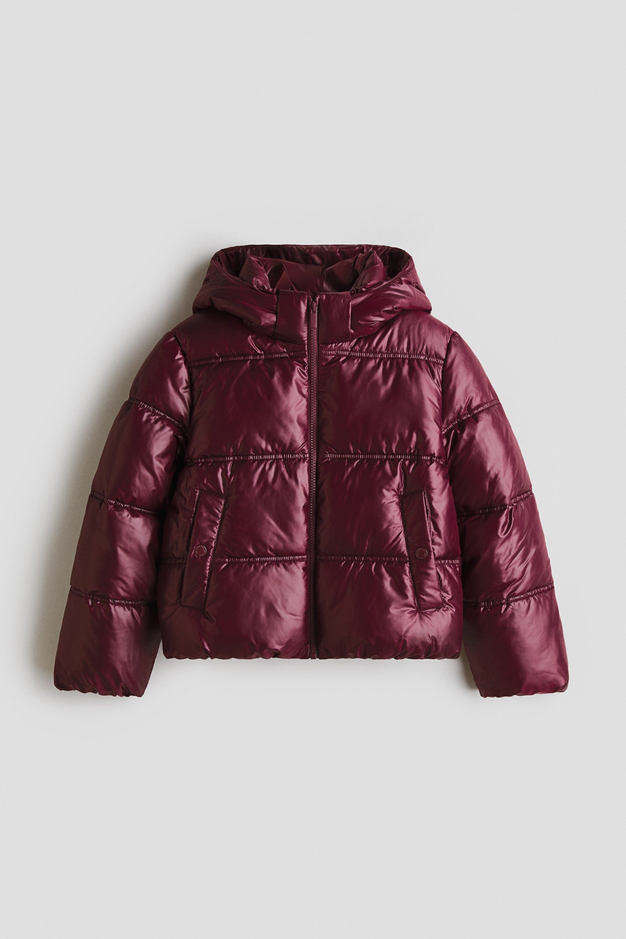 View larger image: A maroon puffer jacket is shown from the front, featuring a quilted weave and a shiny finish. It is designed with a stand collar, an attached hood, a front zip closure, elasticated cuffs, welt front pockets with press-studs, and an elasticated hem.