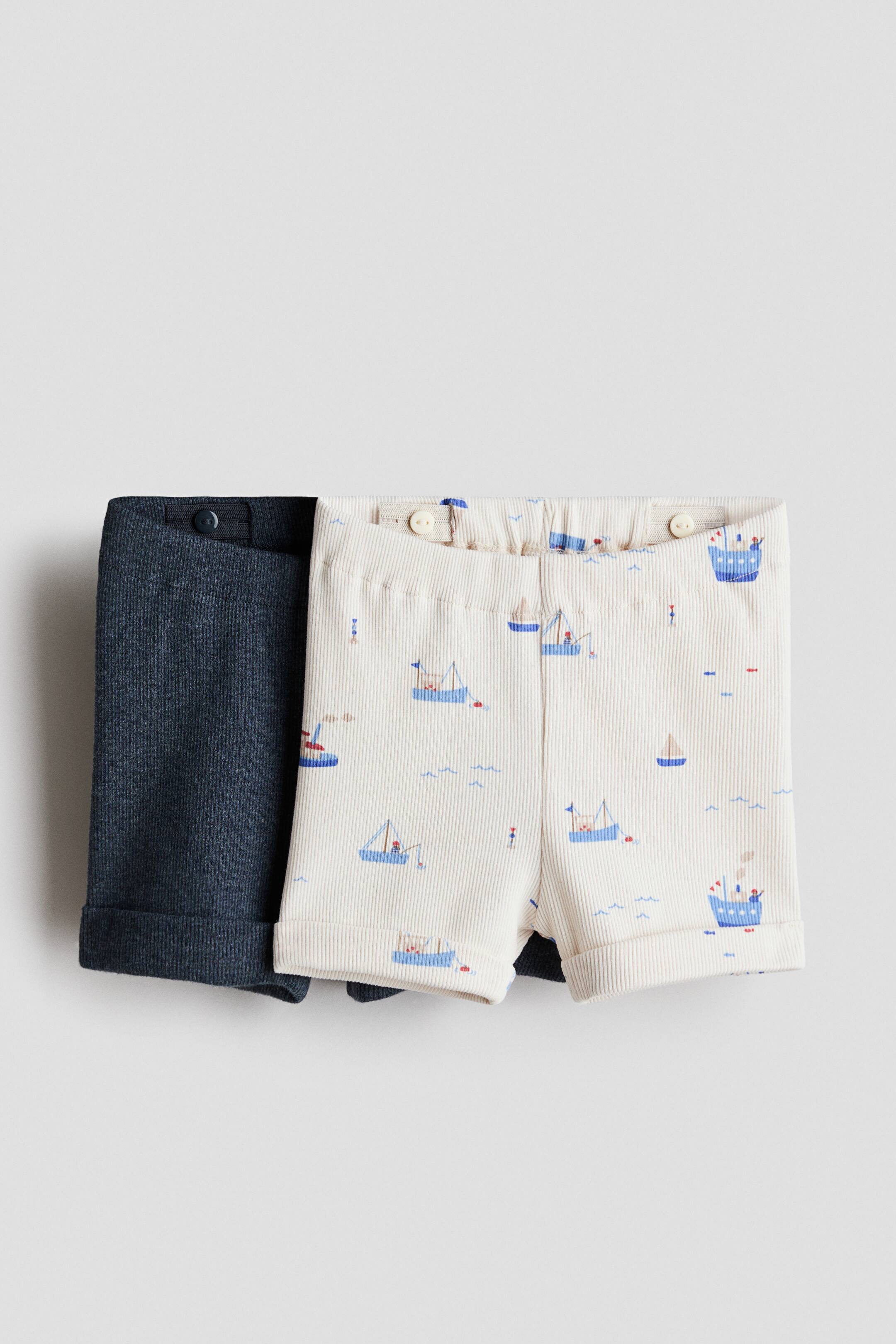 Ver imagem maior: Um conjunto de 2 calções de jersey de algodão está a ser apresentado de frente. Os calções azul escuro canelados são parcialmente visíveis por trás dos calções off-white canelados, que apresentam um padrão de barcos azuis repetidos. Ambos os pares exibem uma cintura elástica com botões internos ajustáveis e punhos das pernas enrolados.