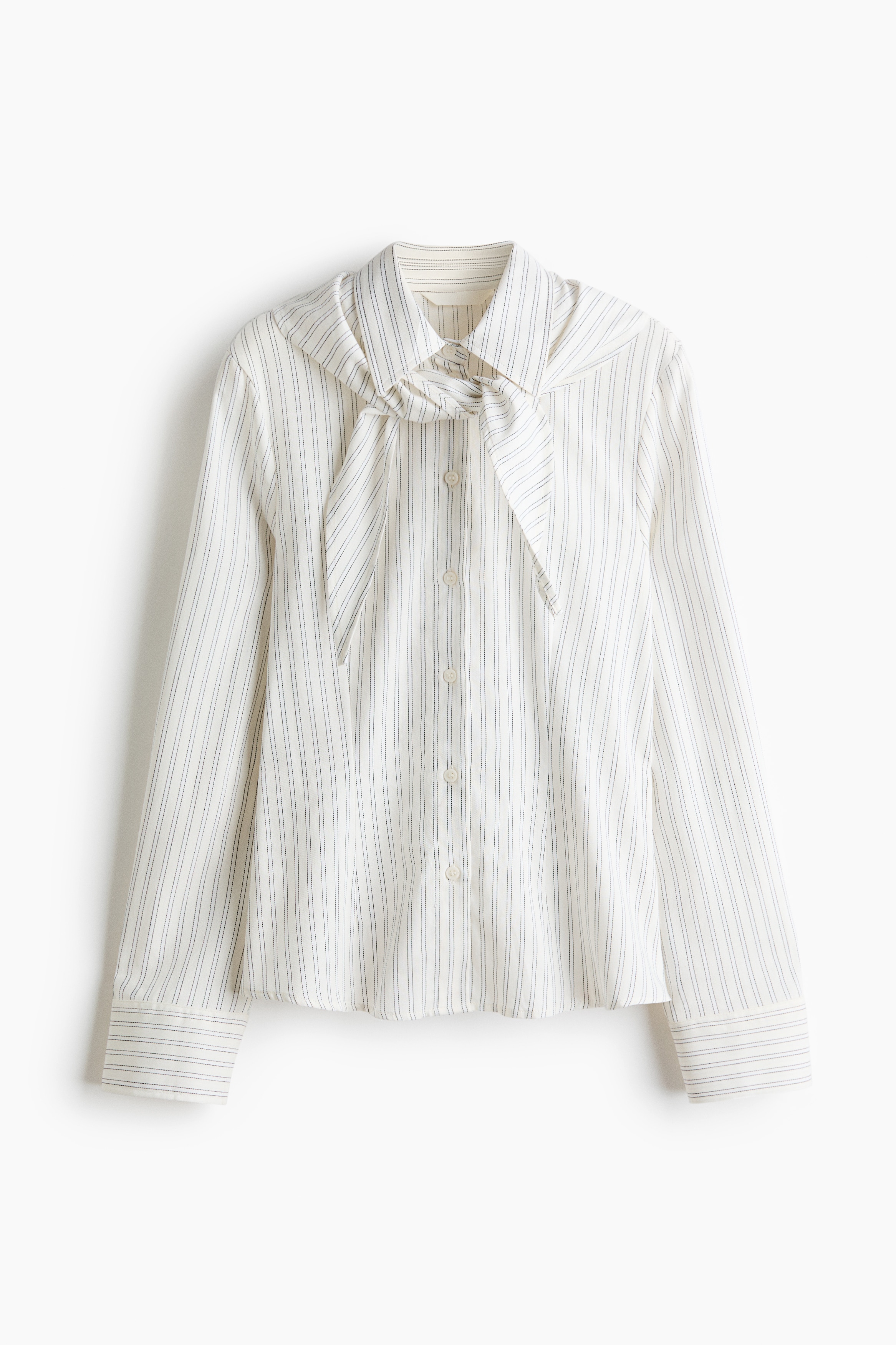 A striped, off-white cotton-weave shirt is being worn by the model, featuring a pointed collar with a matching scarf tied at the neck and buttons down the front.