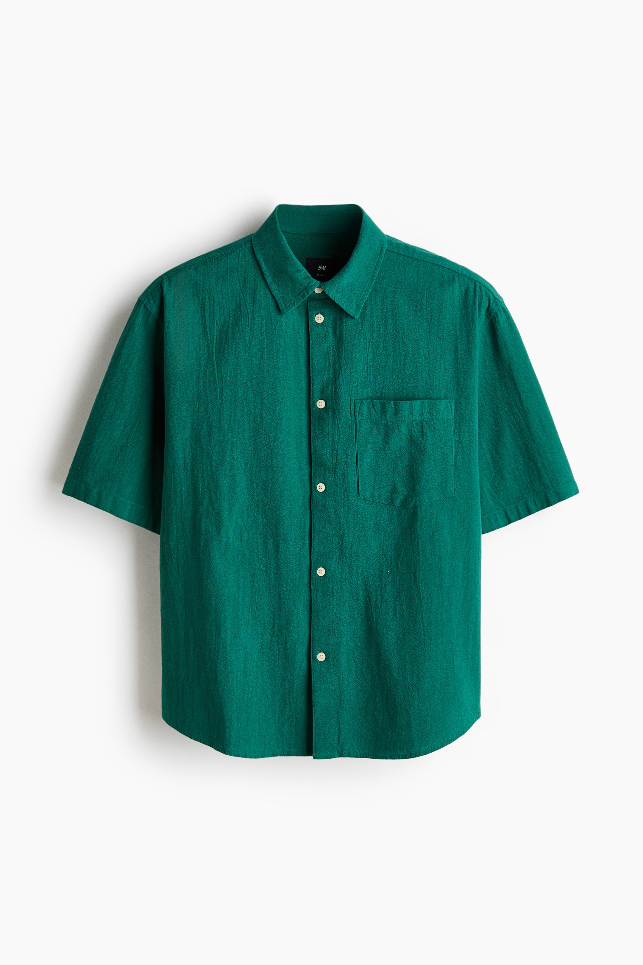 View larger image: A green short-sleeved shirt featuring a textured fabric, a classic collar, and a button-front closure with white buttons. It also showcases a single patch pocket on the left chest and a curved hem.