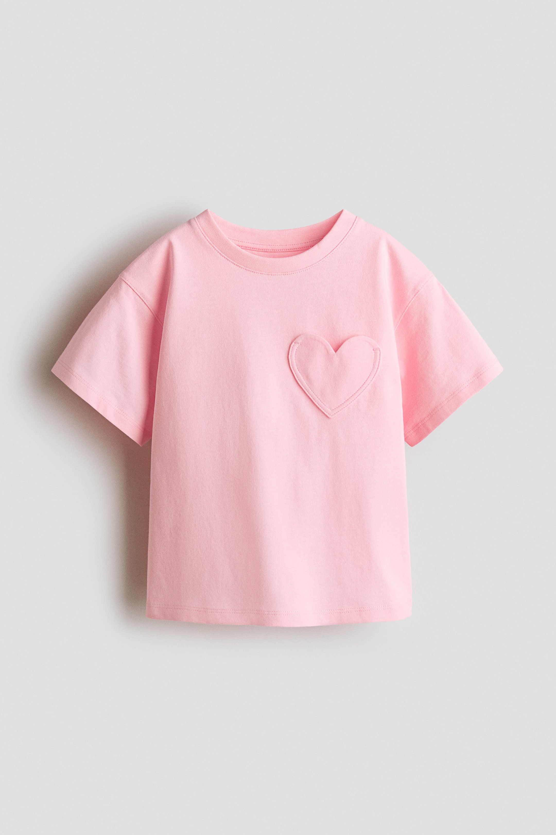 View larger image: A pink t-shirt is shown from the front. It boasts a ribbed crew neck, short sleeves, and a heart-shaped patch pocket on the left chest.