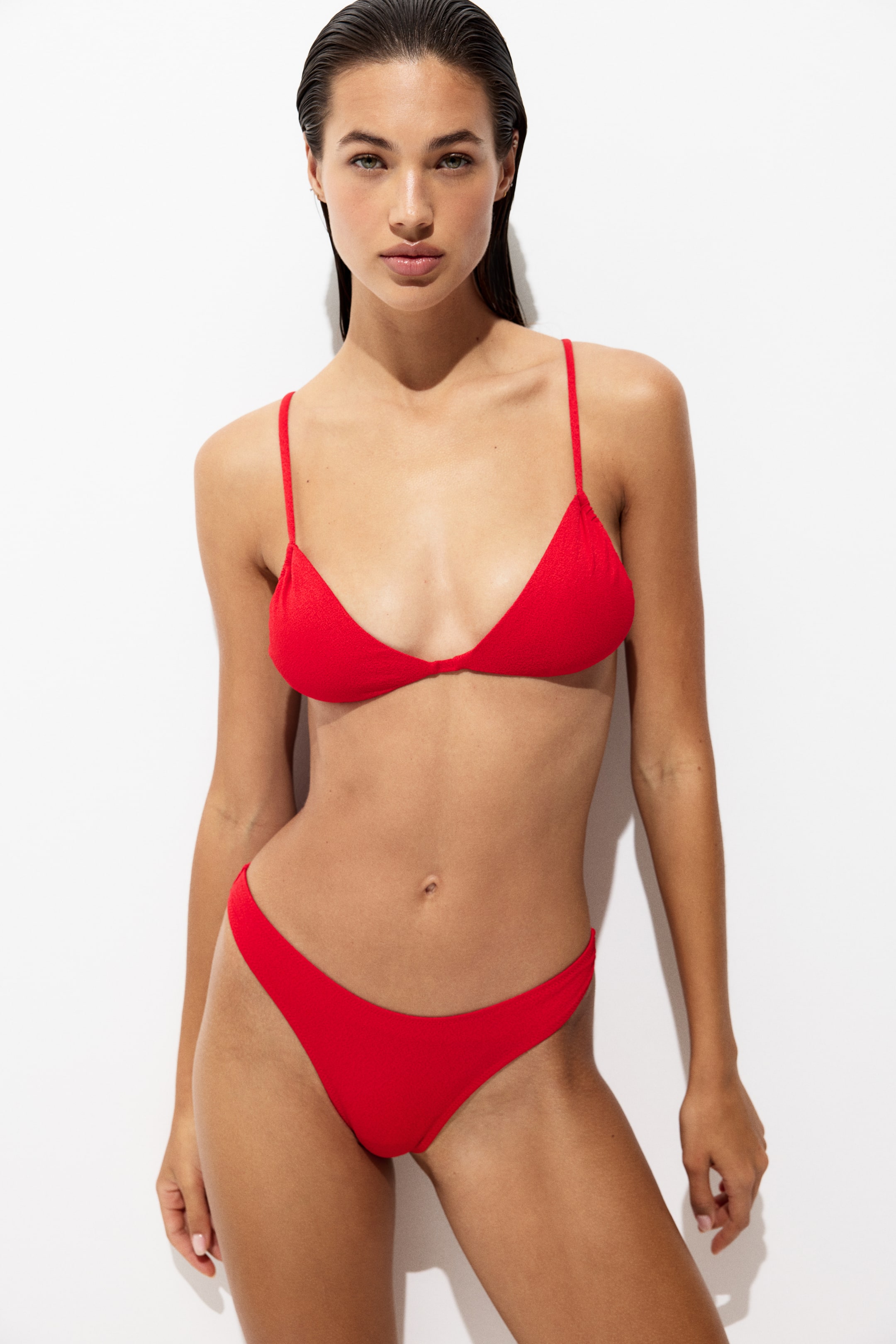 View larger image: A red bikini featuring a triangle top with thin straps and a matching Brazilian-cut bottom, all crafted from subtly textured fabric.