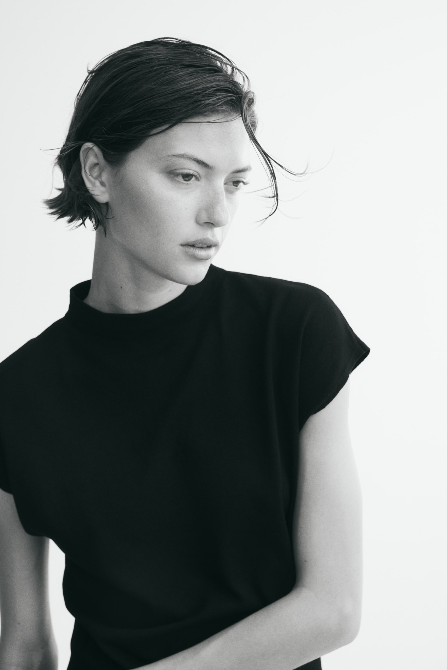 The black sleeveless knit top features a mock neck, cap sleeves, and a ribbed hem, showcased from the front. - 1