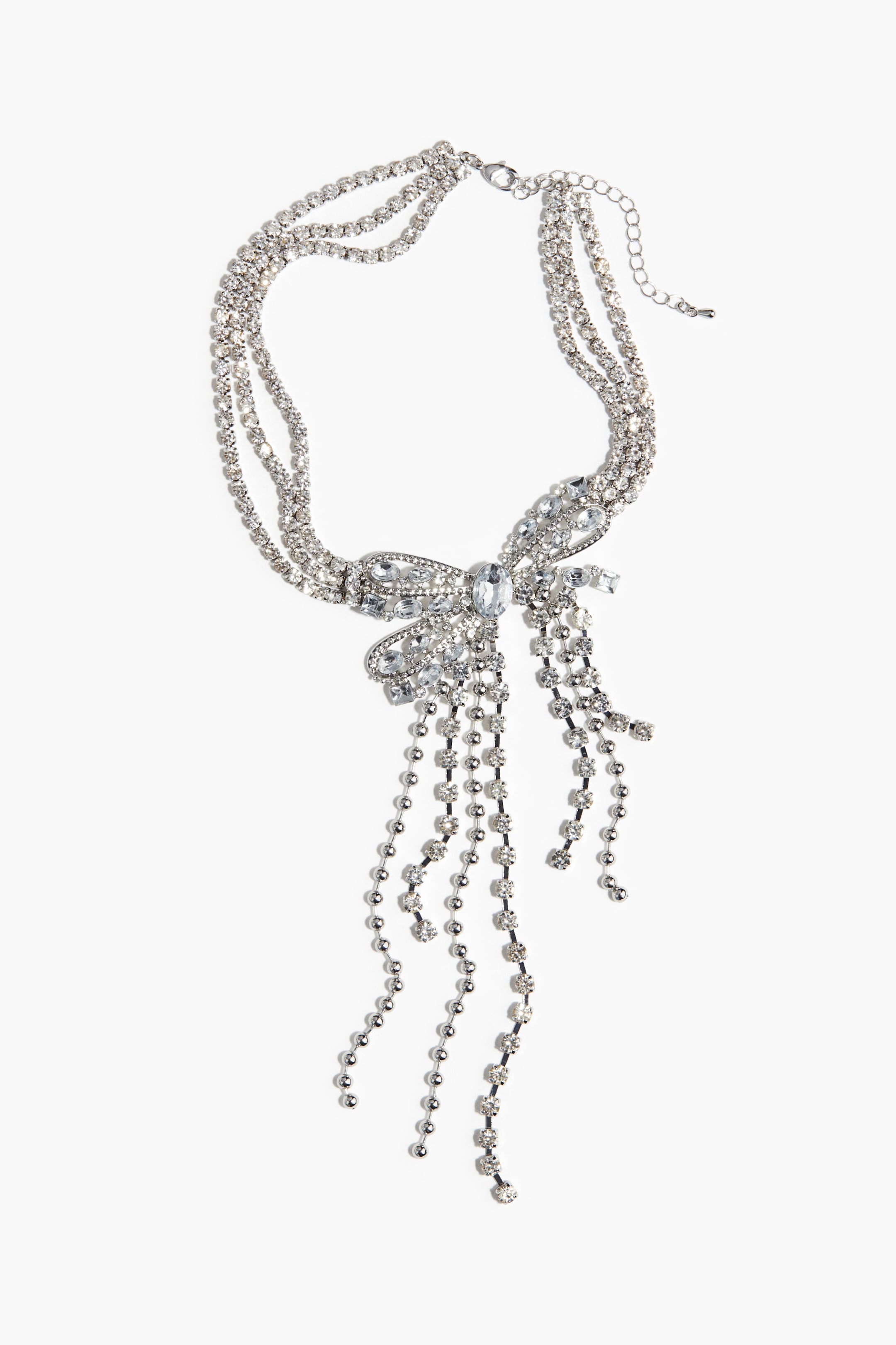 View larger image: A silver-toned multi-strand rhinestone necklace is showcasing a large, rhinestone-encrusted bow centerpiece. Multiple strands of dangling rhinestones and silver-toned beads are extending from the bow, and a lobster clasp with an extender chain is visible at the back.