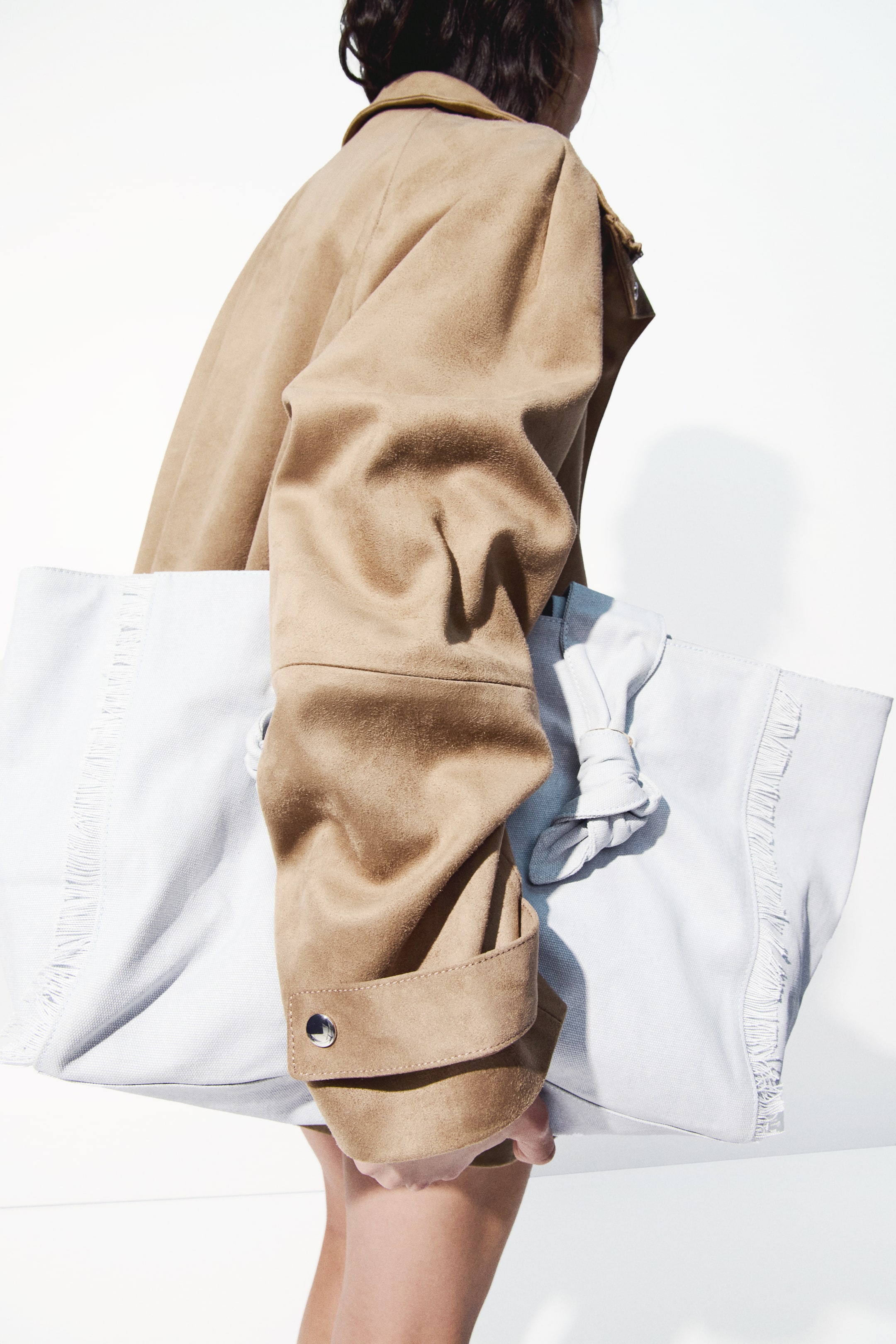 Grösseres Bild ansehen: Eine hellblaue Textil-Tragetasche wird gehalten, die auffällige Fransen entlang ihres oberen Randes und ein geknotetes Griffdetail auf ihrer rechten Seite zeigt.