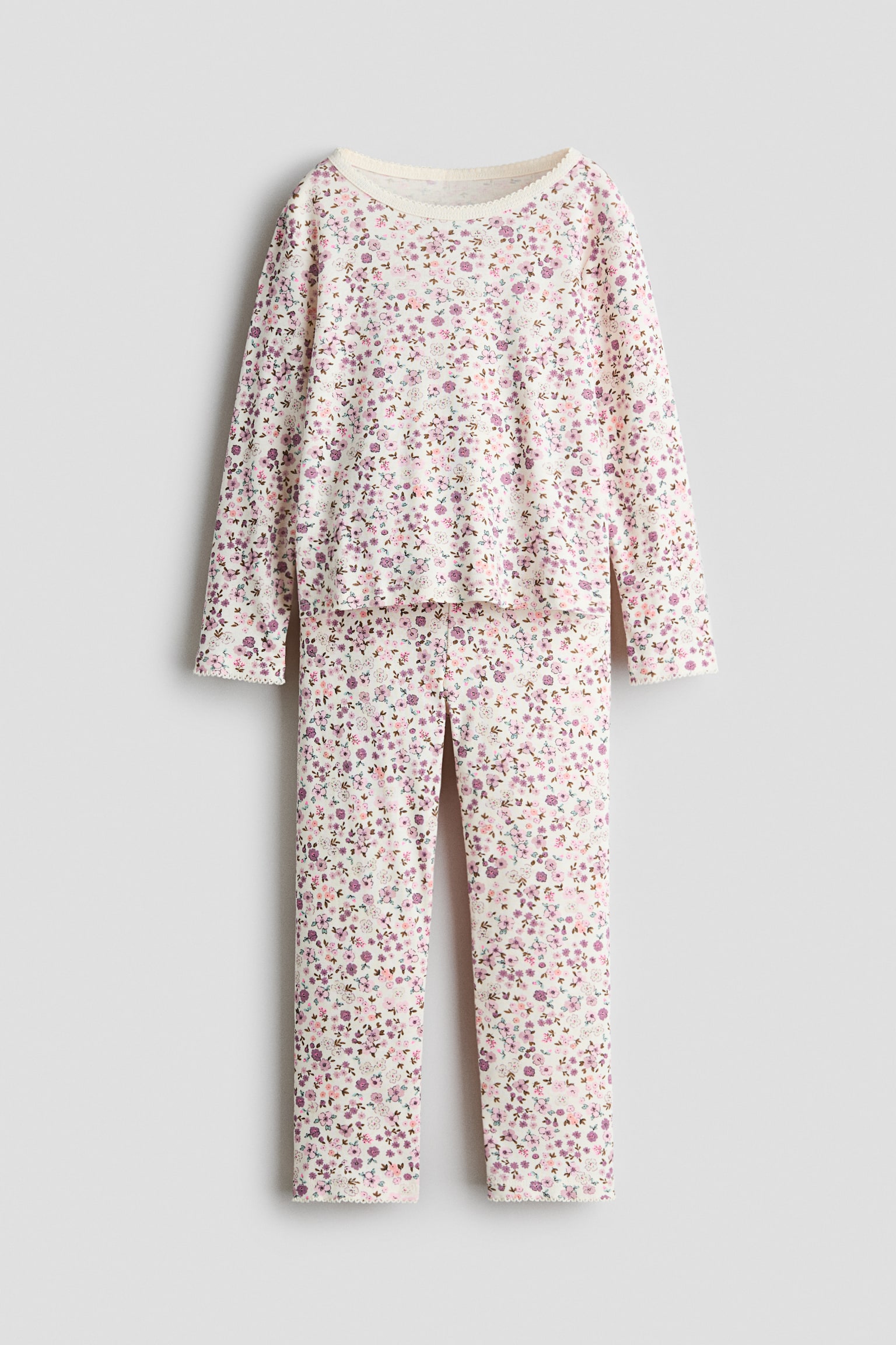 Un ensemble de pyjama est prÃ©sentÃ© de face, composÃ© dâun haut Ã  manches longues et dâun pantalon assorti en tissu de couleur crÃ¨me, avec un imprimÃ© floral violet et rose sur lâensemble. Le haut est dotÃ© dâun col rond, et les deux piÃ¨ces sont finies avec une dÃ©licate bordure picot au niveau de lâencolure, des poignets et des ourlets.