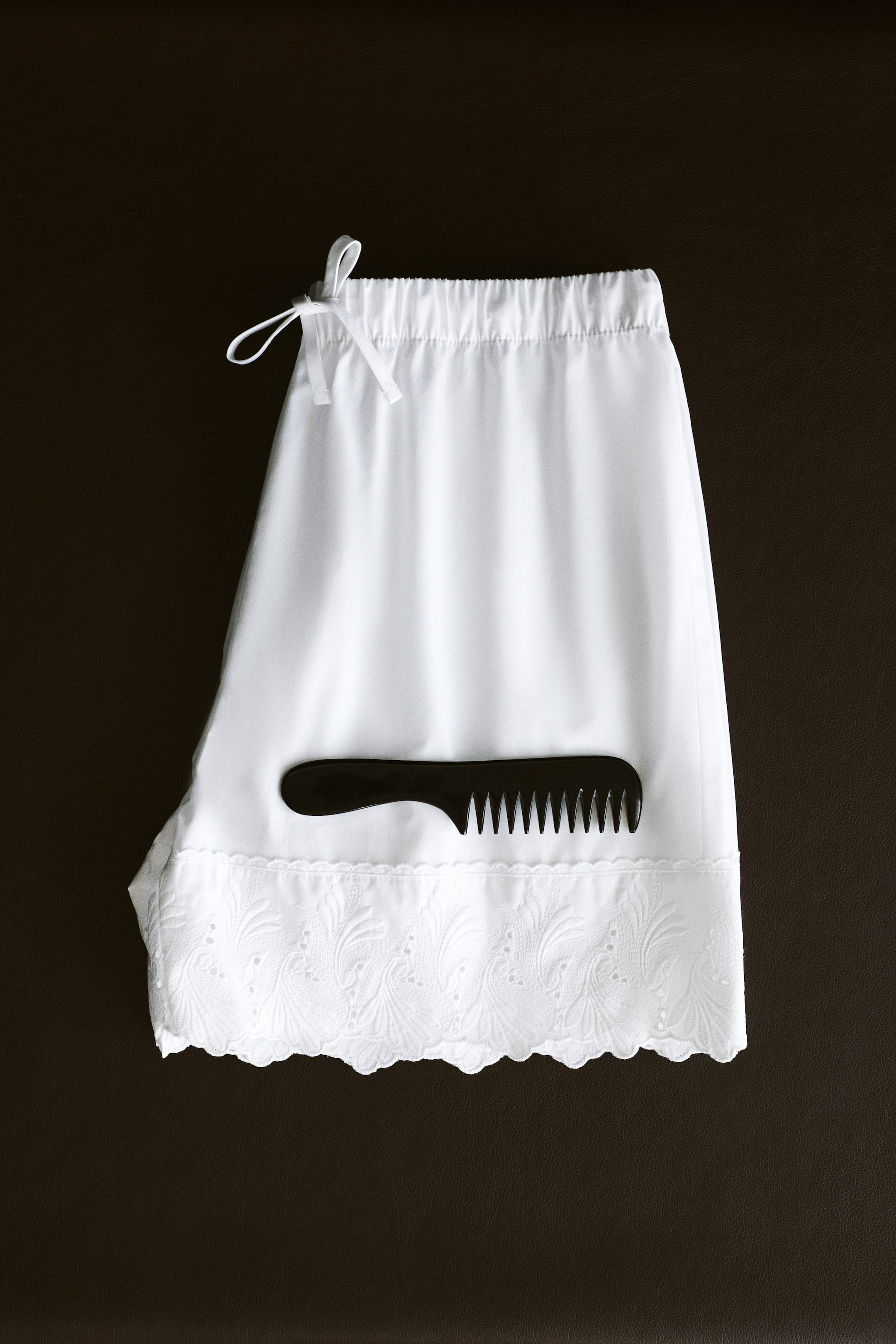 View larger image: White cotton pajama shorts are laid flat, facing front. They feature an elasticized drawstring waistband tied in a bow and a wide scalloped hem with broderie anglaise.
